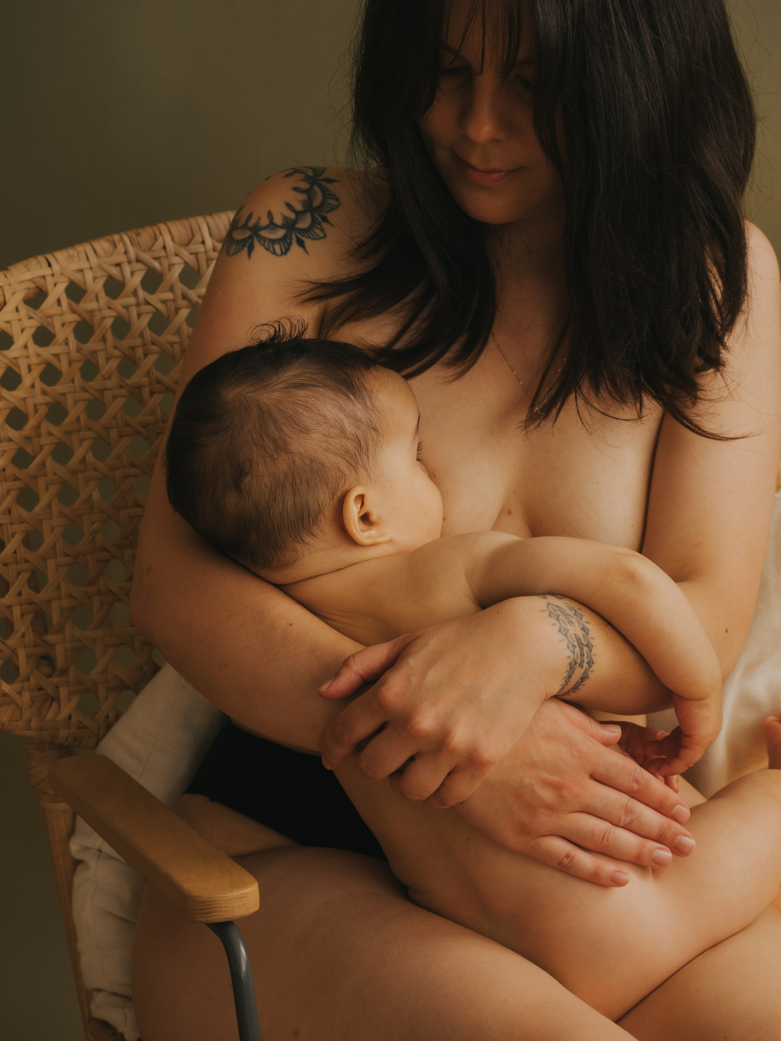 Woman breastfeeding in front of an olive-colored background.