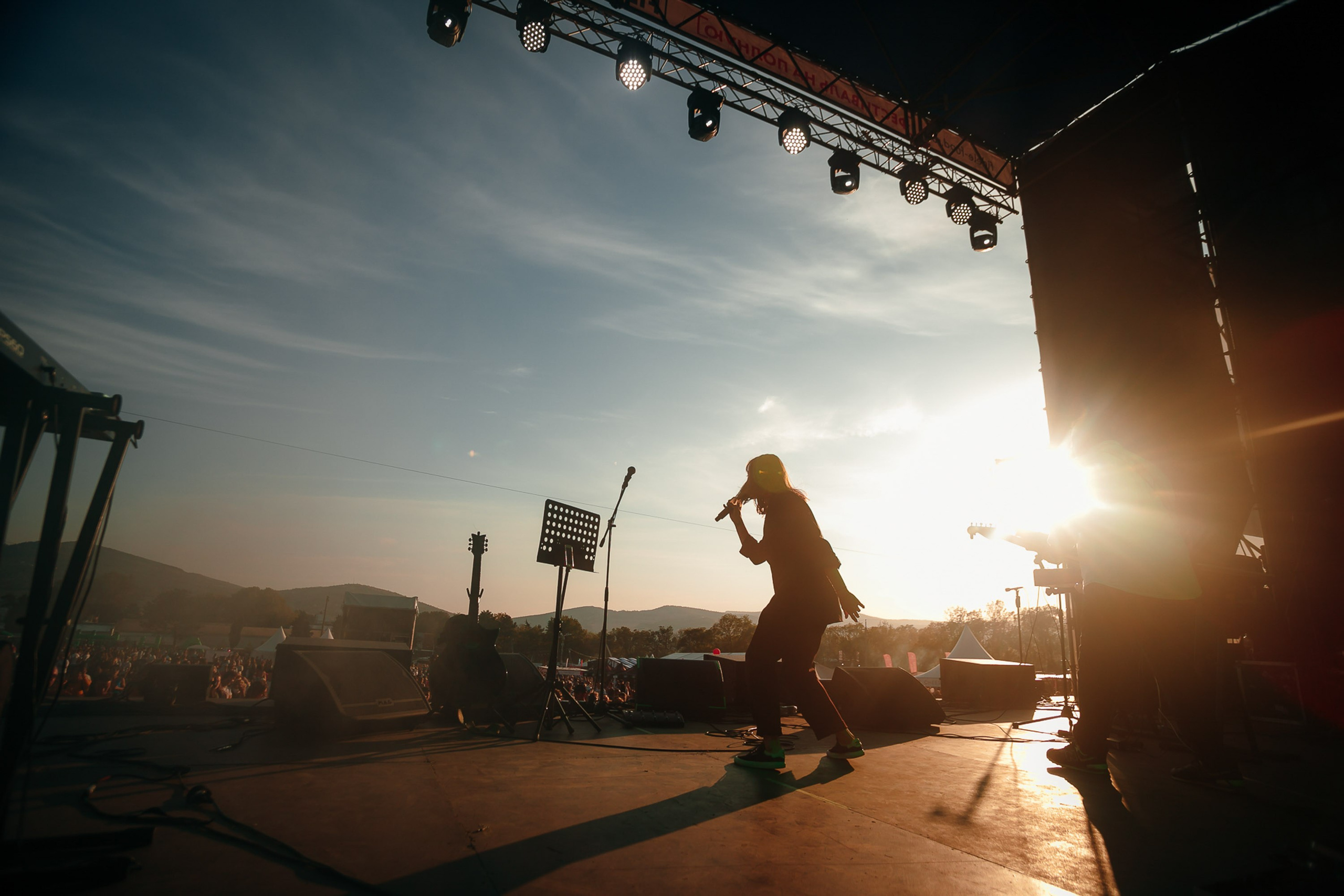 Singer performing on outdoor stage, sun flare