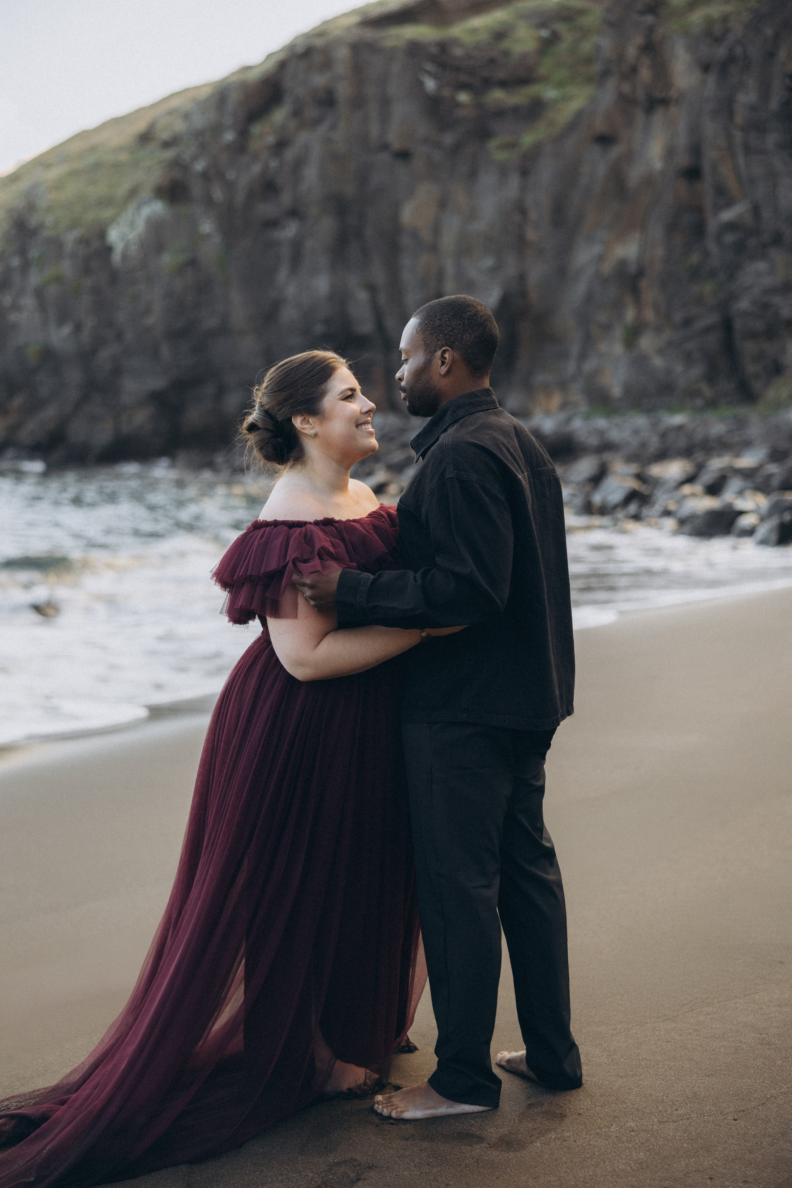 A glowing expectant mother standing on a cliff overlooking the ocean in Madeira, her dress flowing gently in the wind as the golden sunset casts a warm glow.