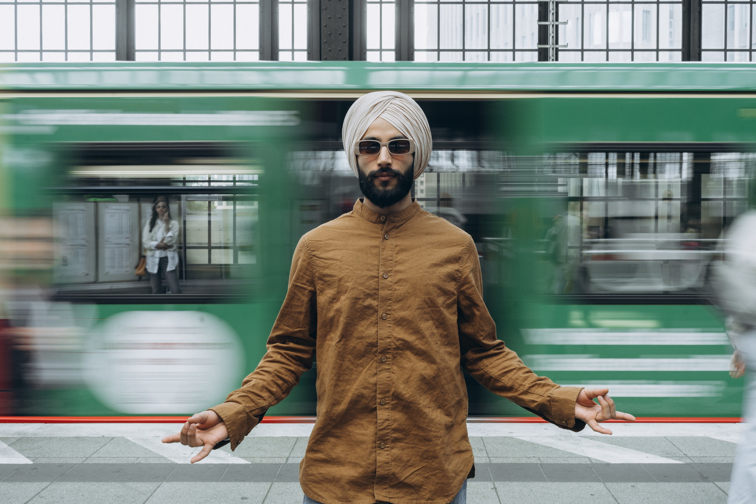 Mann mit Turban posiert auf der Straße, vorbeifahrende Straßenbahn im Hintergrund – urbanes Portraitshooting