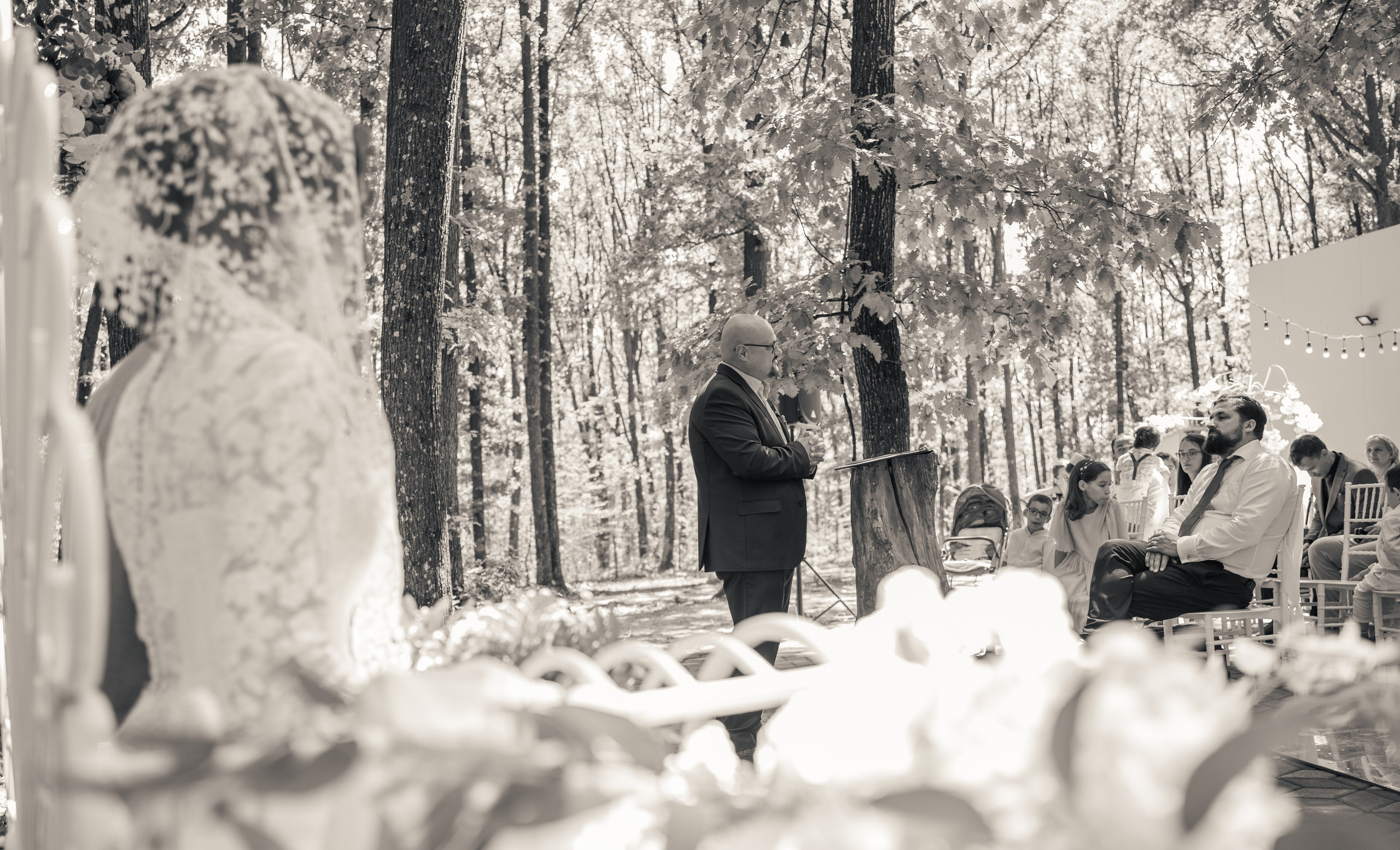 Ceremonie de nuntă în aer liber alb-negru, mireasă cu văl de dantelă privind spre oficiant, nuntă în pădure București, fotografie stil documentar, incadru.ro.
