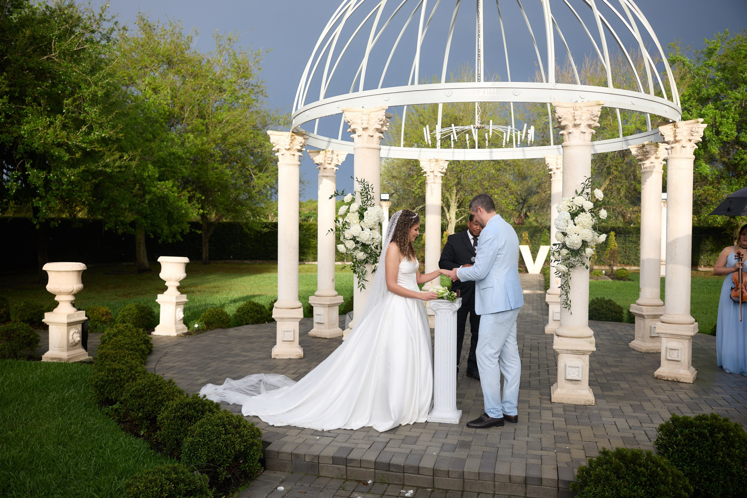Wide view of an outdoor wedding ceremony beneath a white gazebo