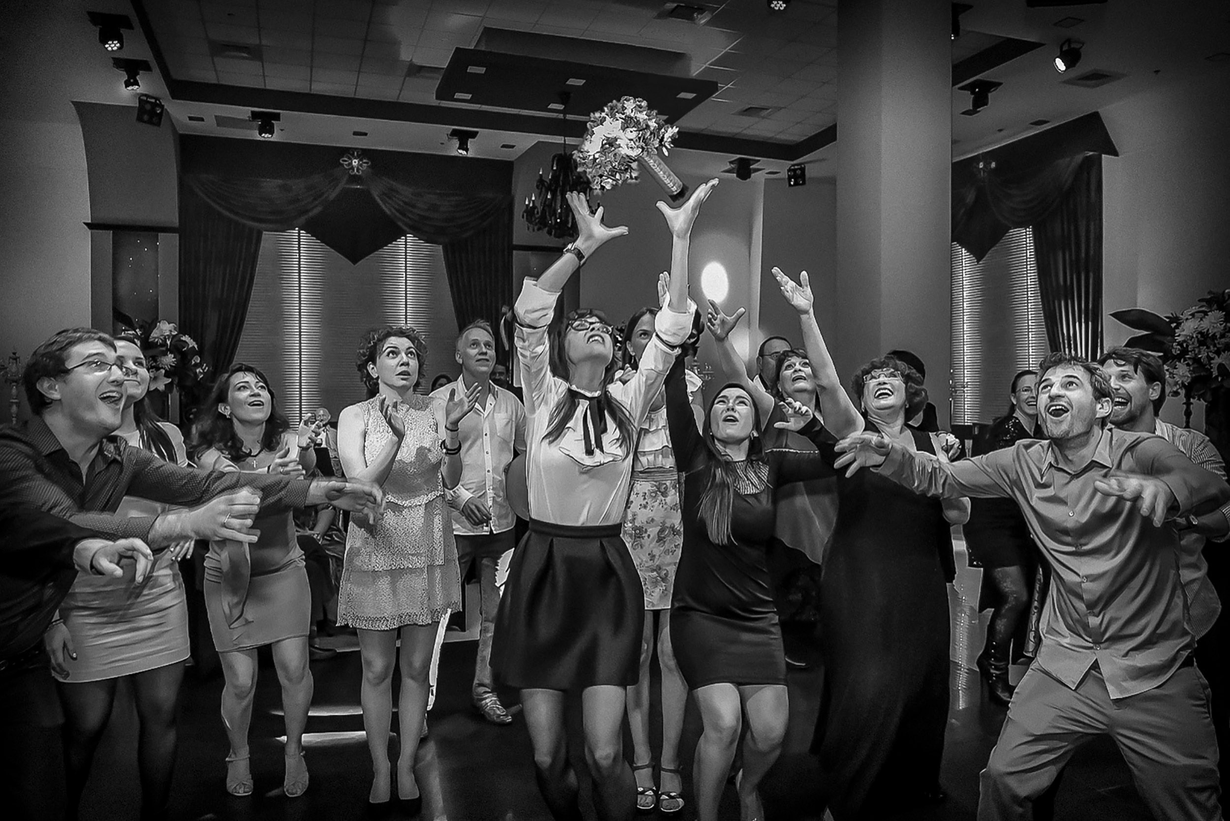 Wedding guests reach for a bridal bouquet flying above them