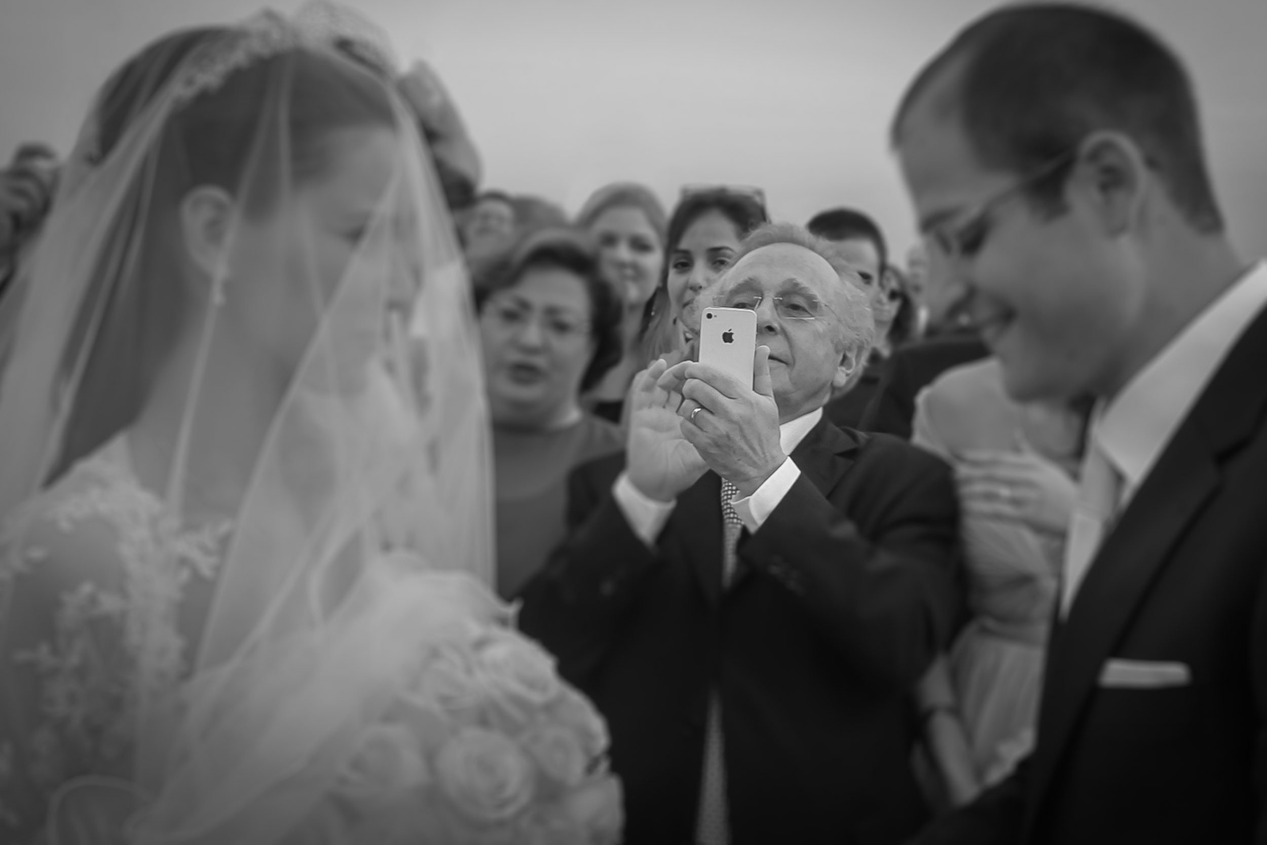 An older man photographs the bride and groom with his phone during the wedding ceremony