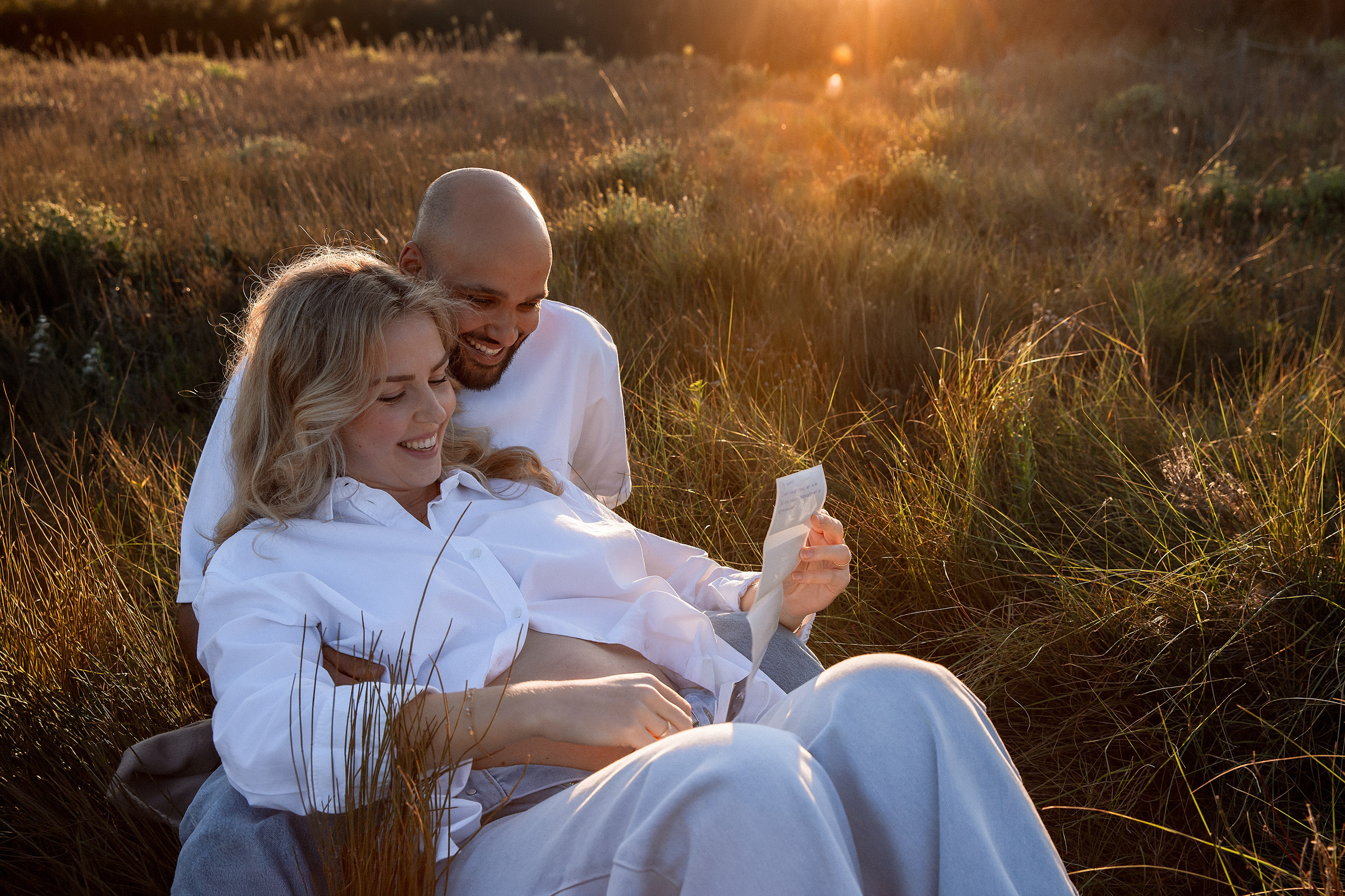 Sesión de fotos de embarazo en Valencia, España, con una pareja relajándose junta en un cálido campo al atardecer, con la pareja abrazando suavemente a la mujer embarazada, capturada durante la hora dorada — ideal para fotografía romántica de embarazo en Valencia y España.