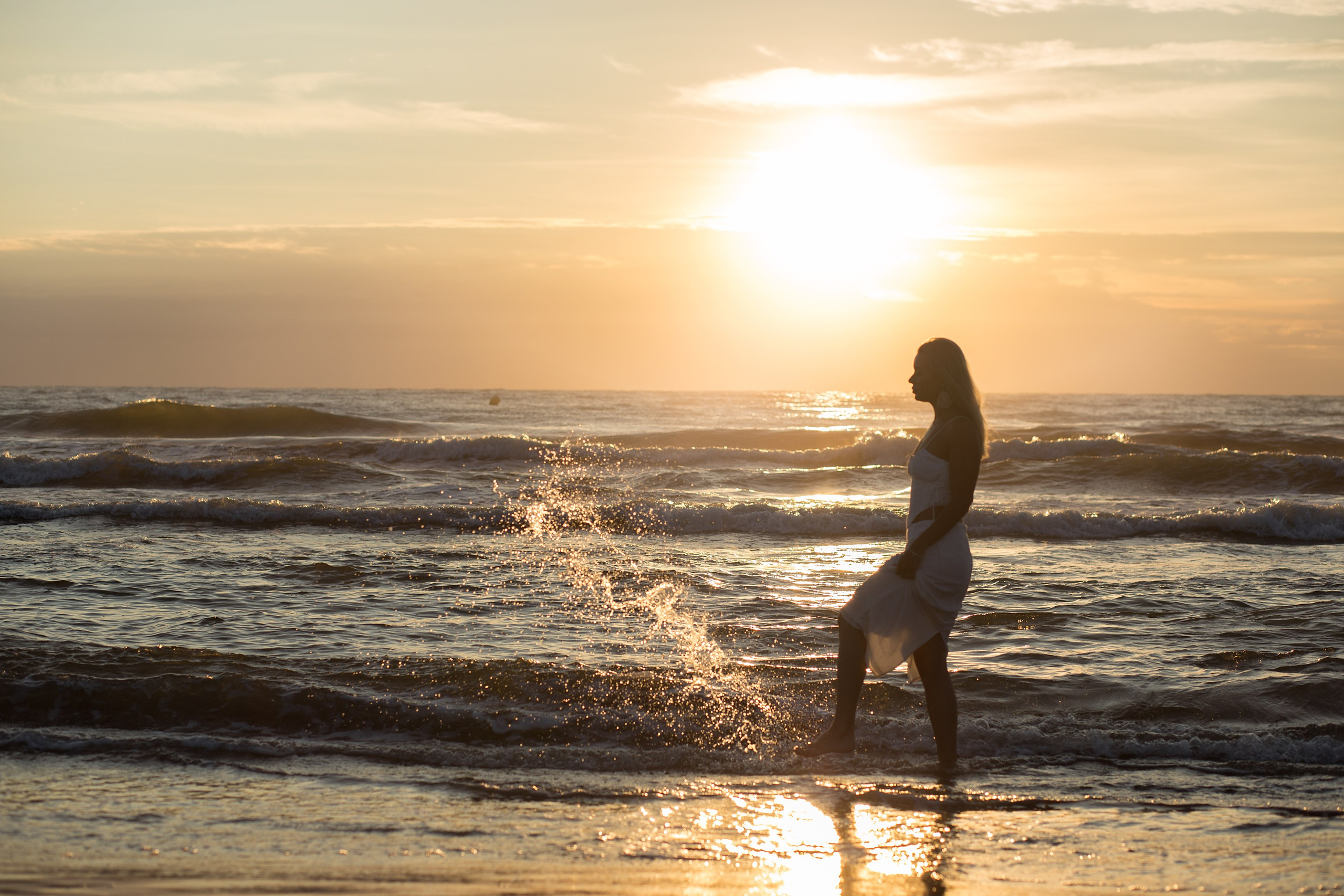 Портрет женщины в белом платье, идущей вдоль берега на закате, с волнами, омывающими ее ноги, в Валенсии, Испания