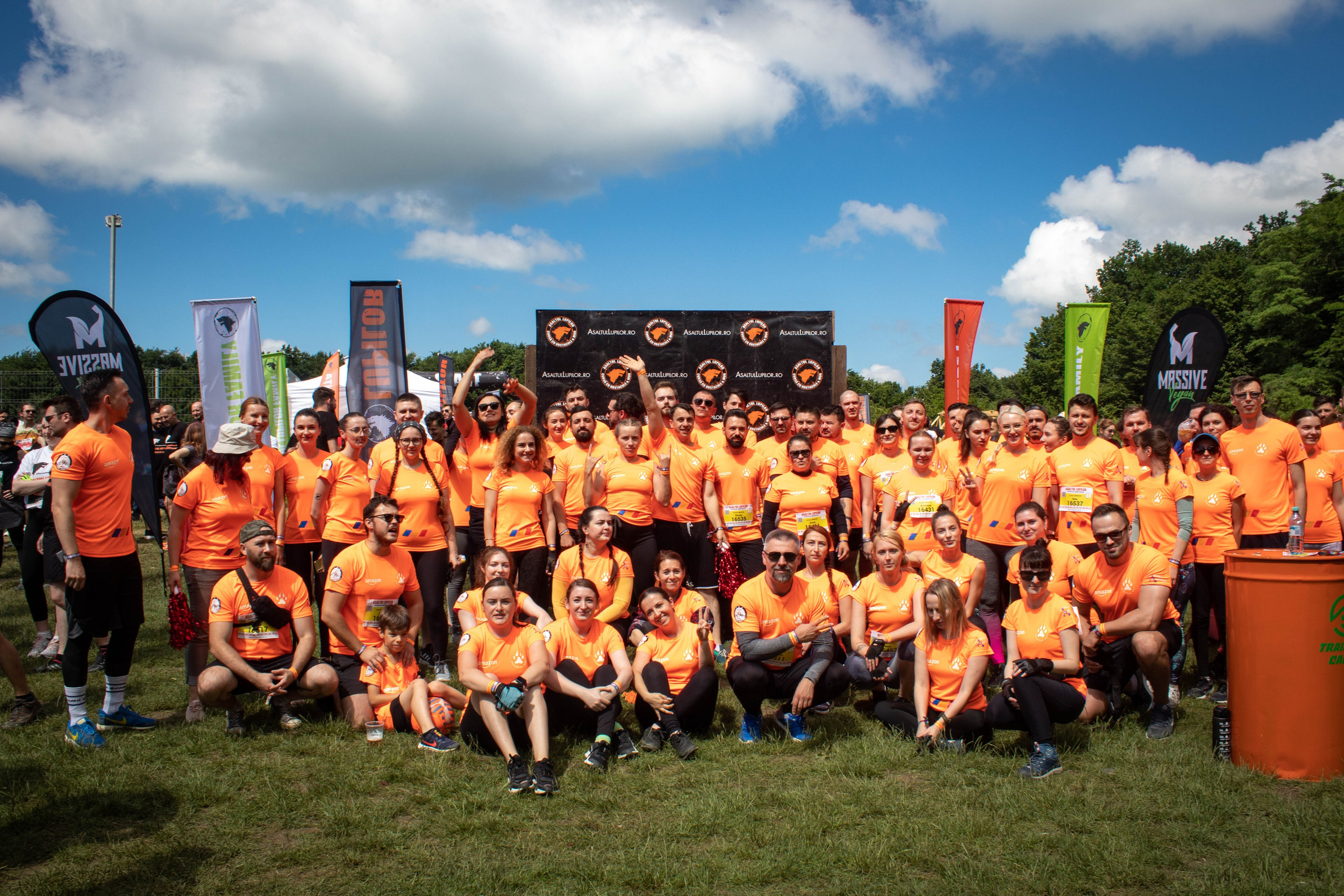 Large group of athletes wearing orange shirts posing together after an outdoor race.