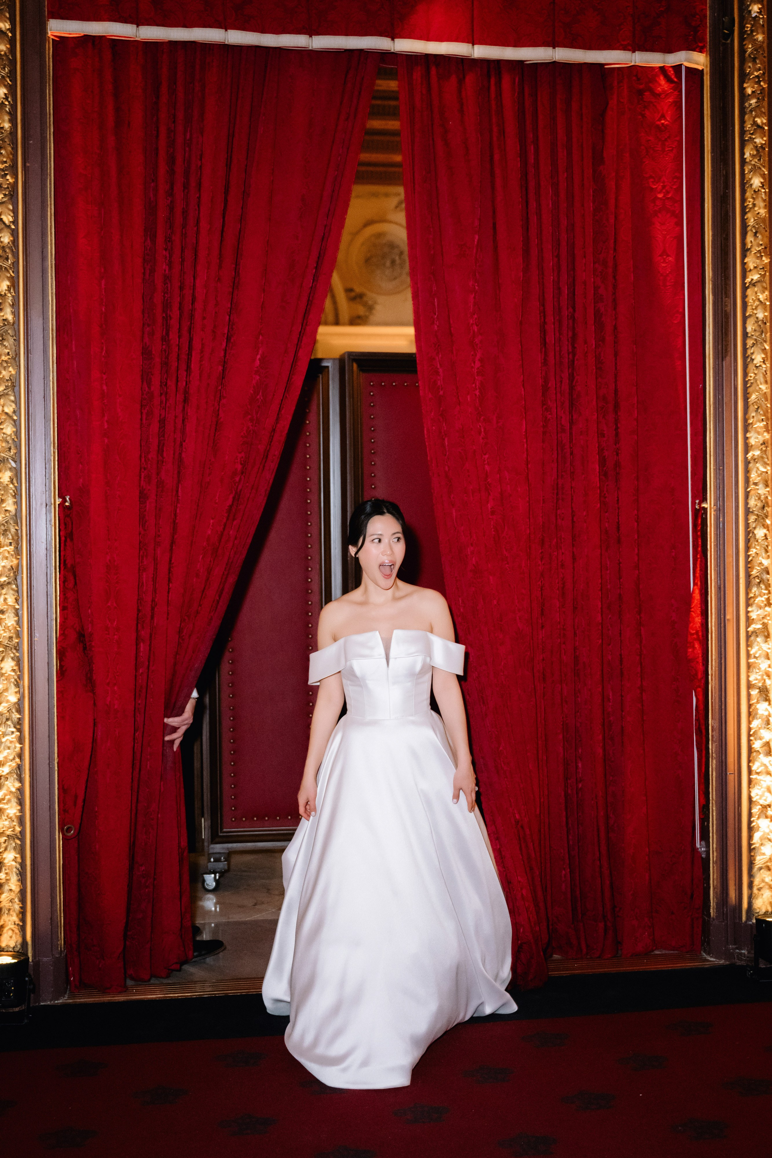 a woman in a white dress standing in front of a red curtain