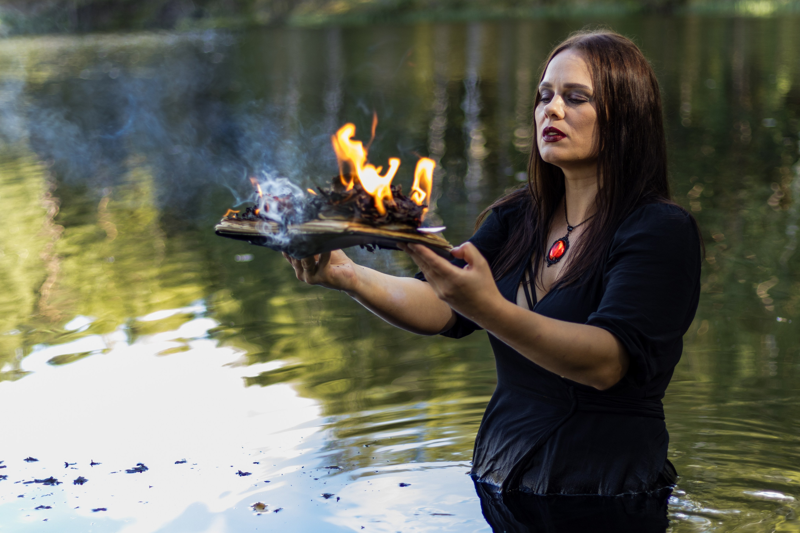 Девушка-ведьма в черном одеянии держит горящую книгу в руках.