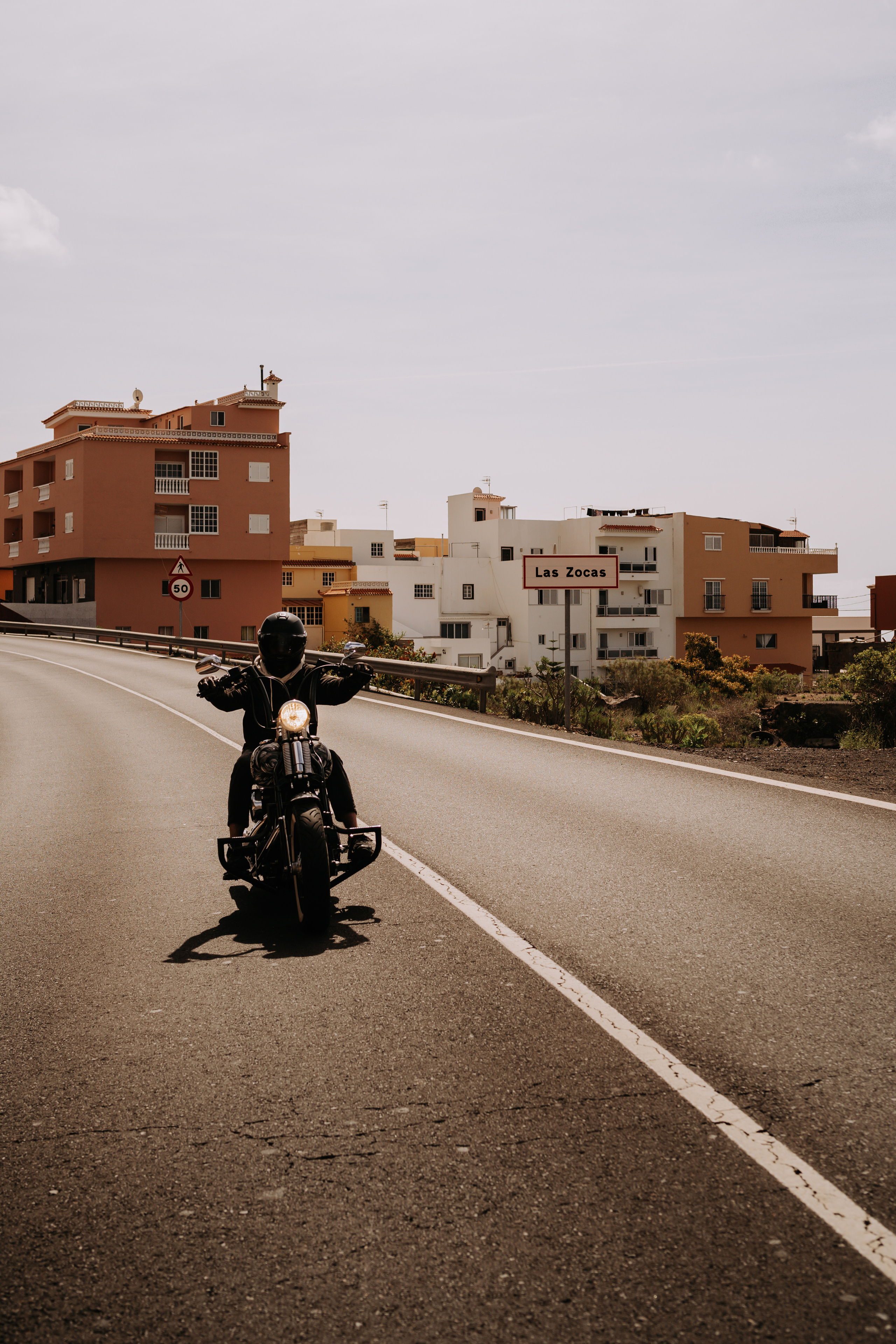 A lone motorcycle rider cruising down an empty road in a small town under clear skies, conveying solitude and freedom.