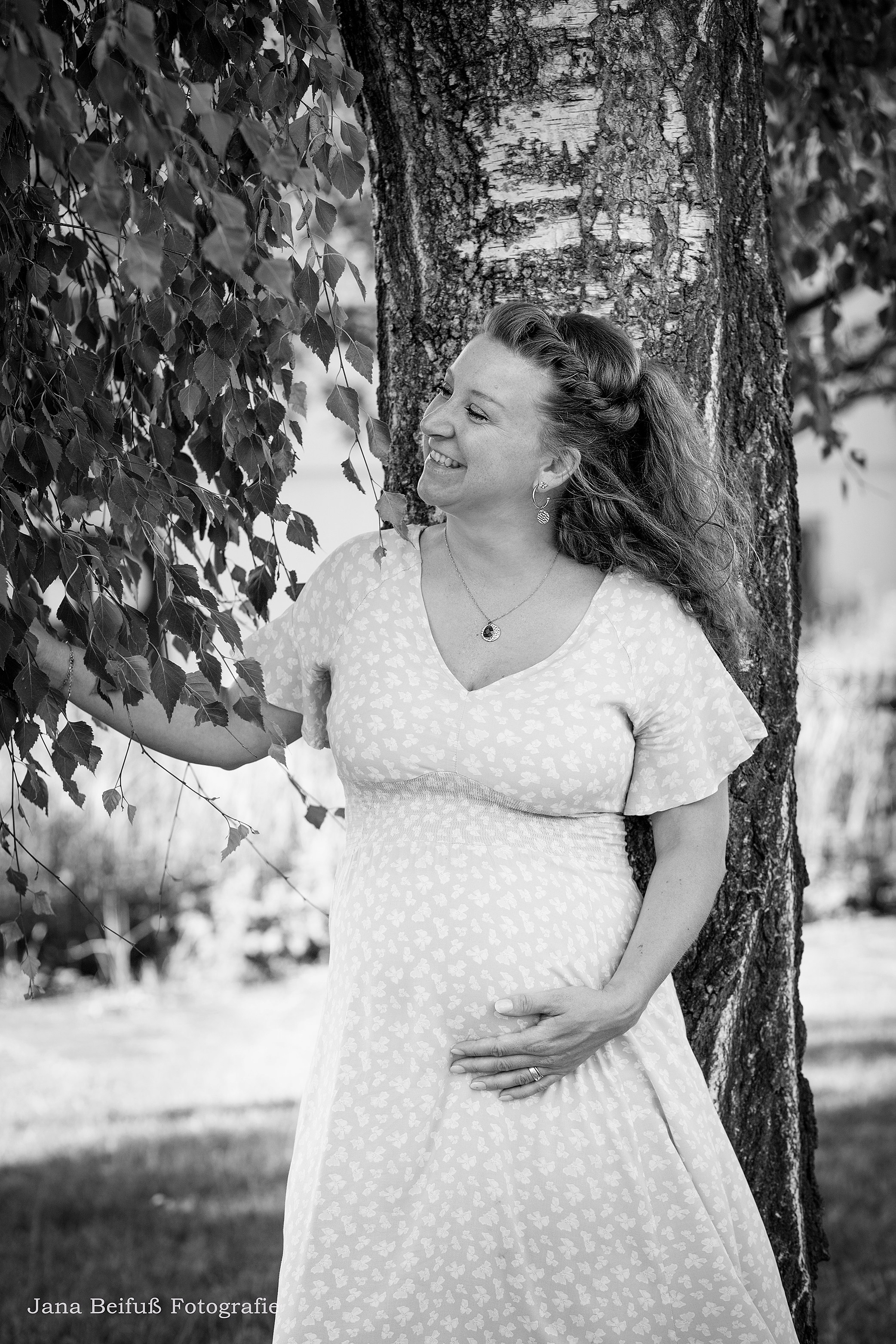 glückliche werdende Mama steht am Birkenbaum und schaut glücklich - Schwangerschaftsfotograf Jana Beifuß in Weißenhorn bei Ulm 