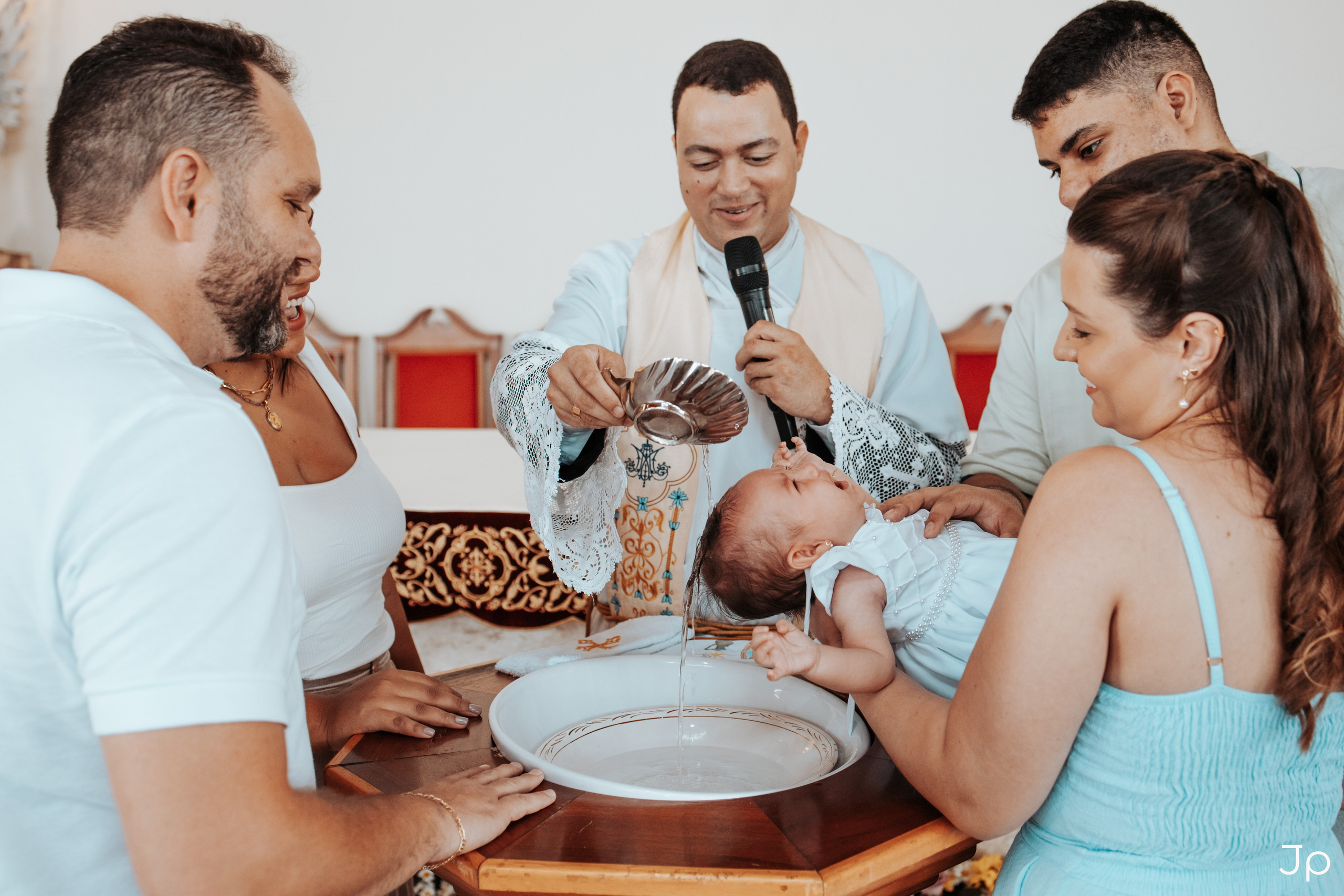 Pais e sacerdote reunidos ao redor da pia batismal.