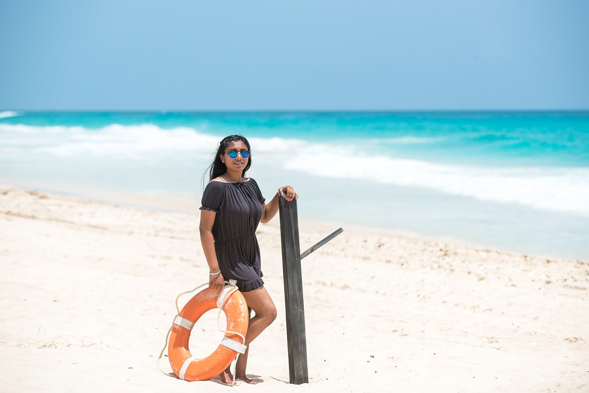 Woman in a flowing dress posing on a white sand beach during a Punta Cana photoshoot.