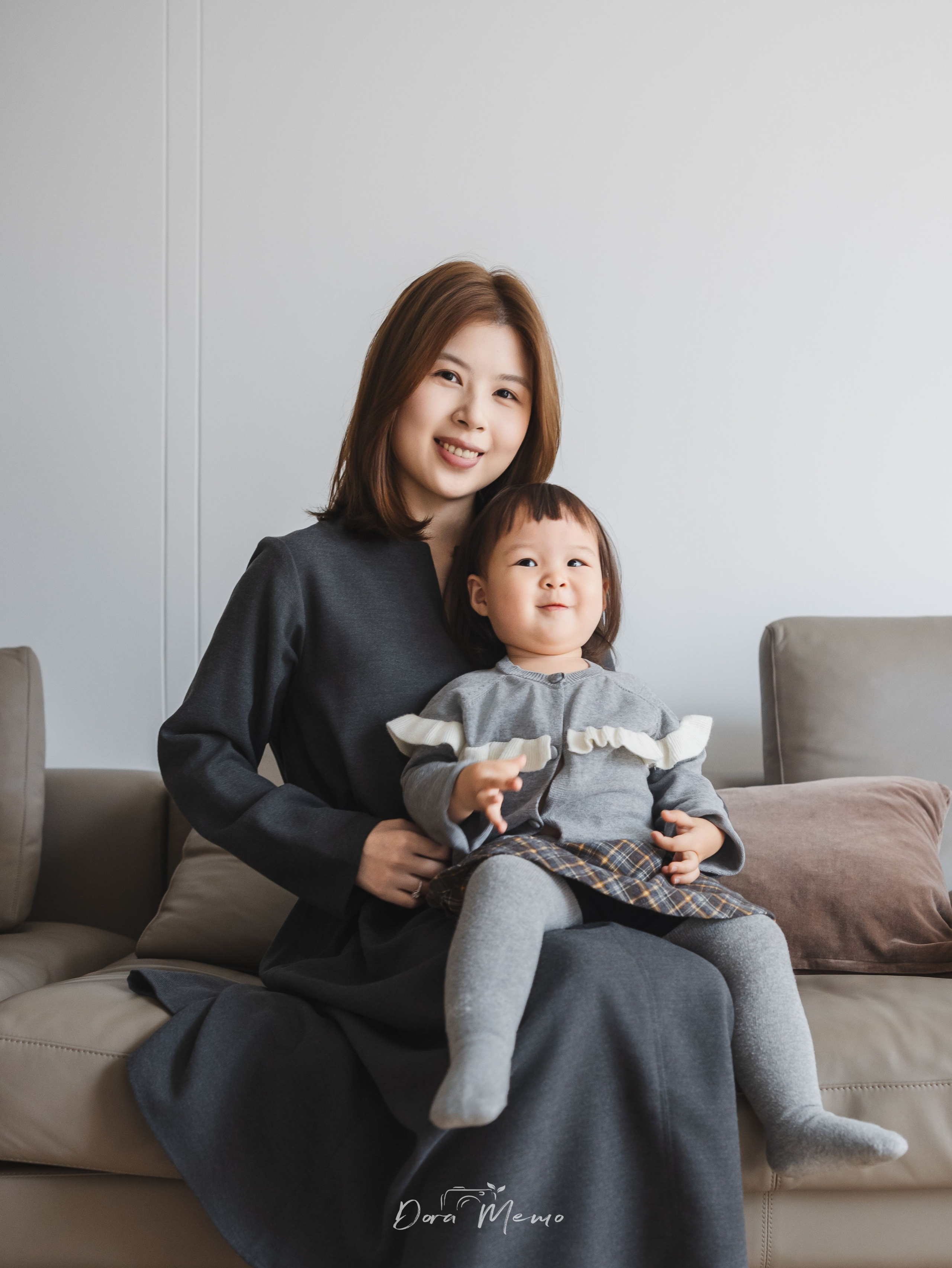 Mother cradling her two-year-old daughter on the sofa in a quiet moment, gentle family bonding captured by a Shanghai lifestyle photographer.