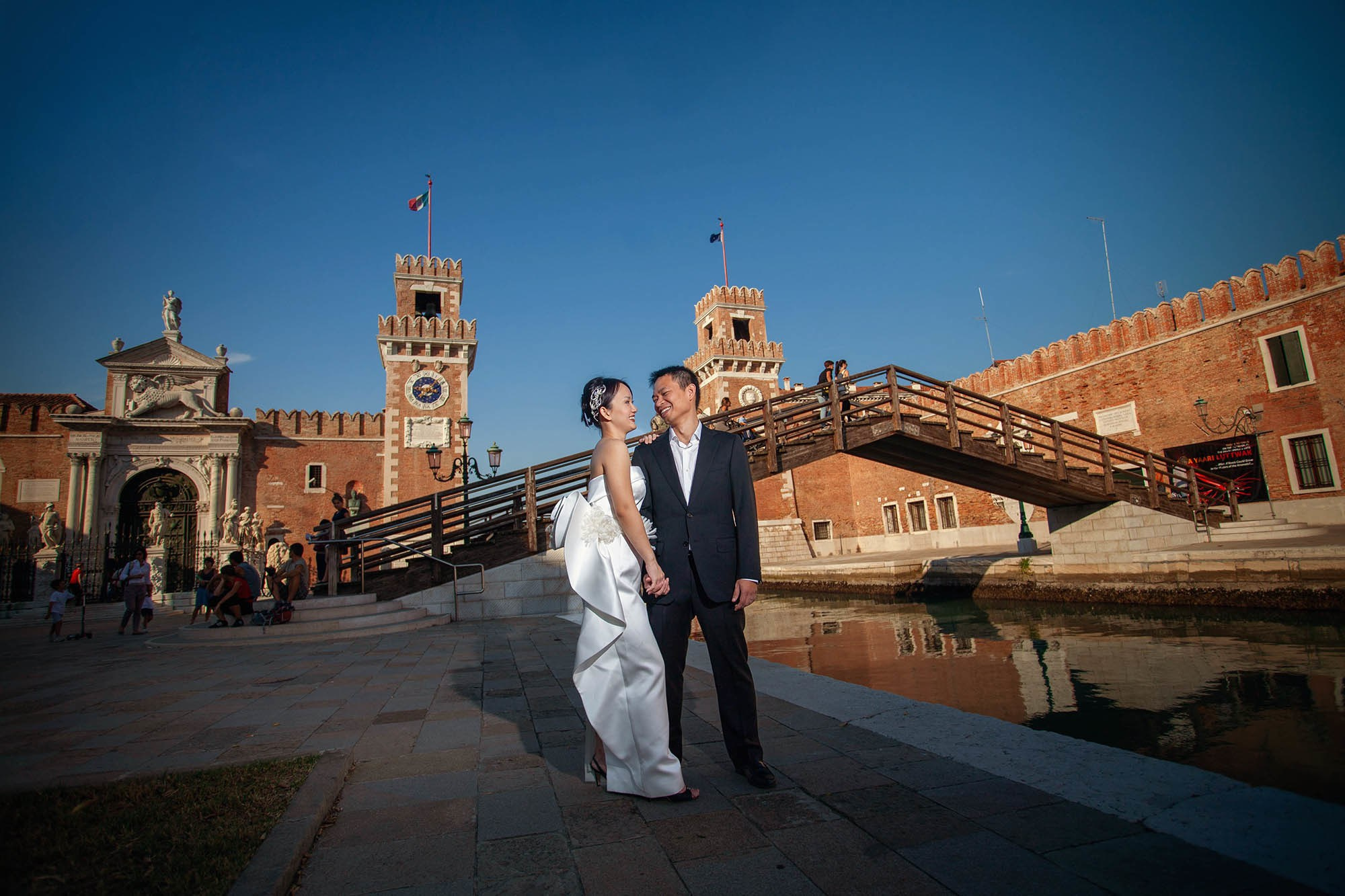 Thai bride in profile embracing groom in front of historic Venetian Arsenal gate.