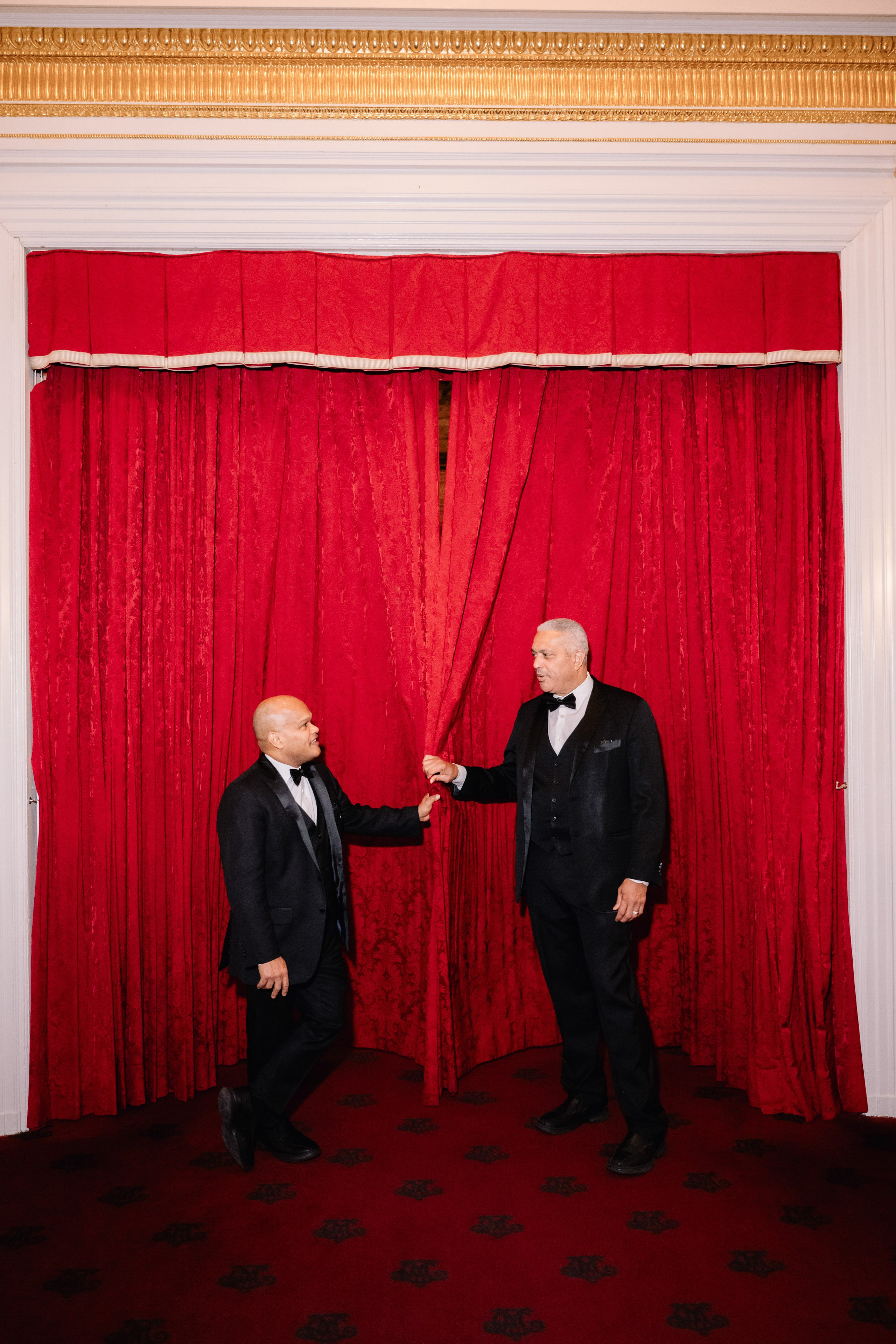 two men in tuxed suits are standing in front of a red curtain