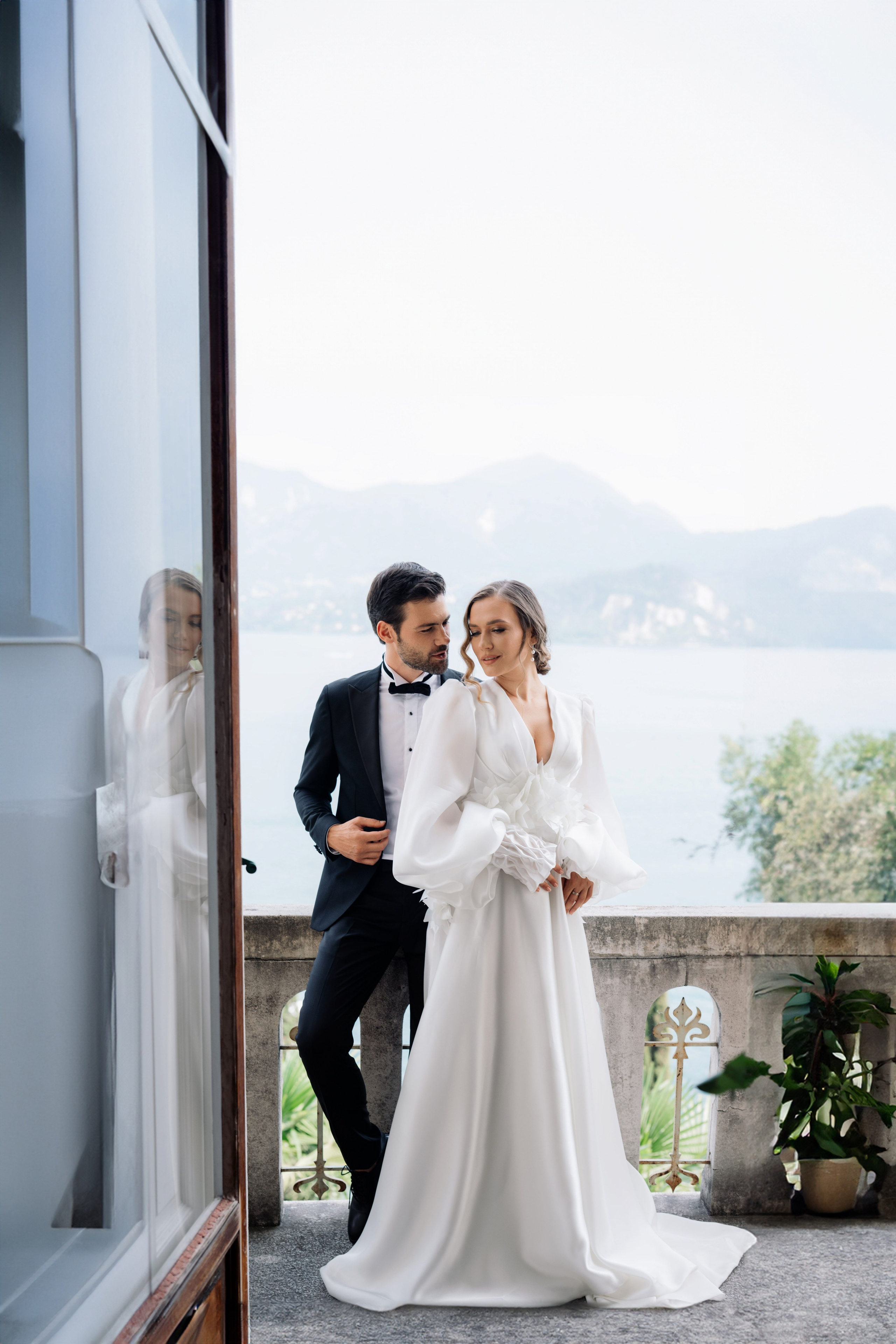 a bride and groom pose for a photo in front of a window