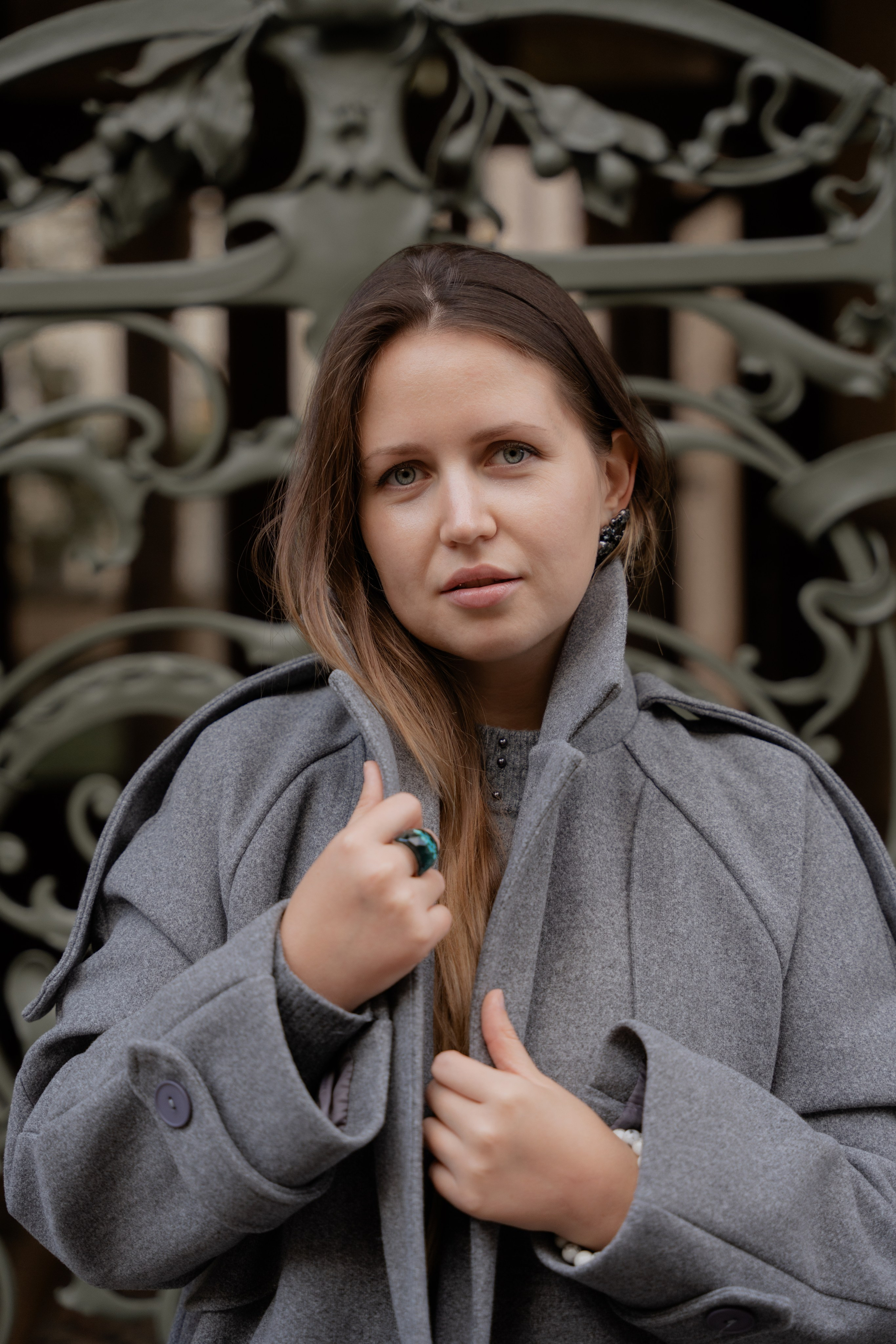 На фото девушка в сером пальто на фоне зеленой кованной решетки в стиле либерти в Милане