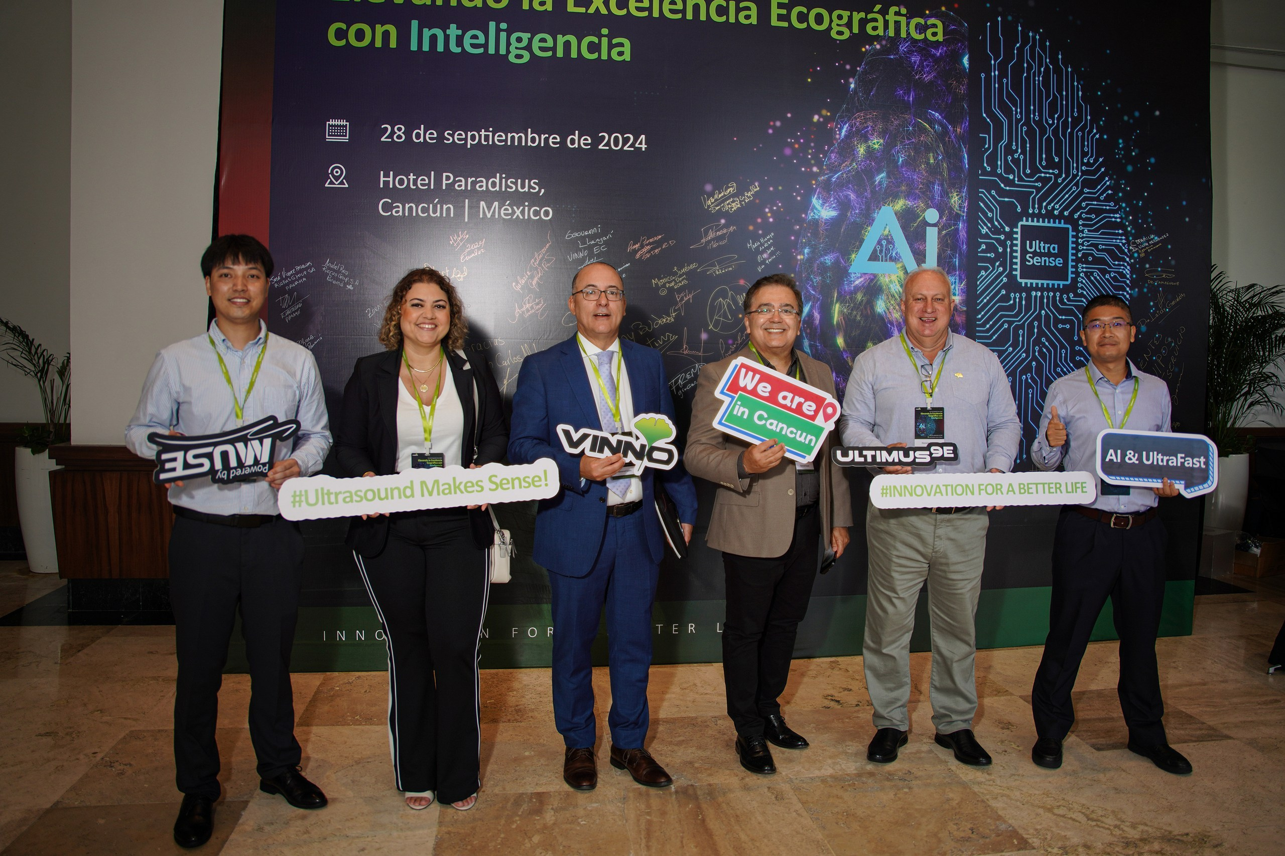 Group of event participants posing together in front of branded wall.