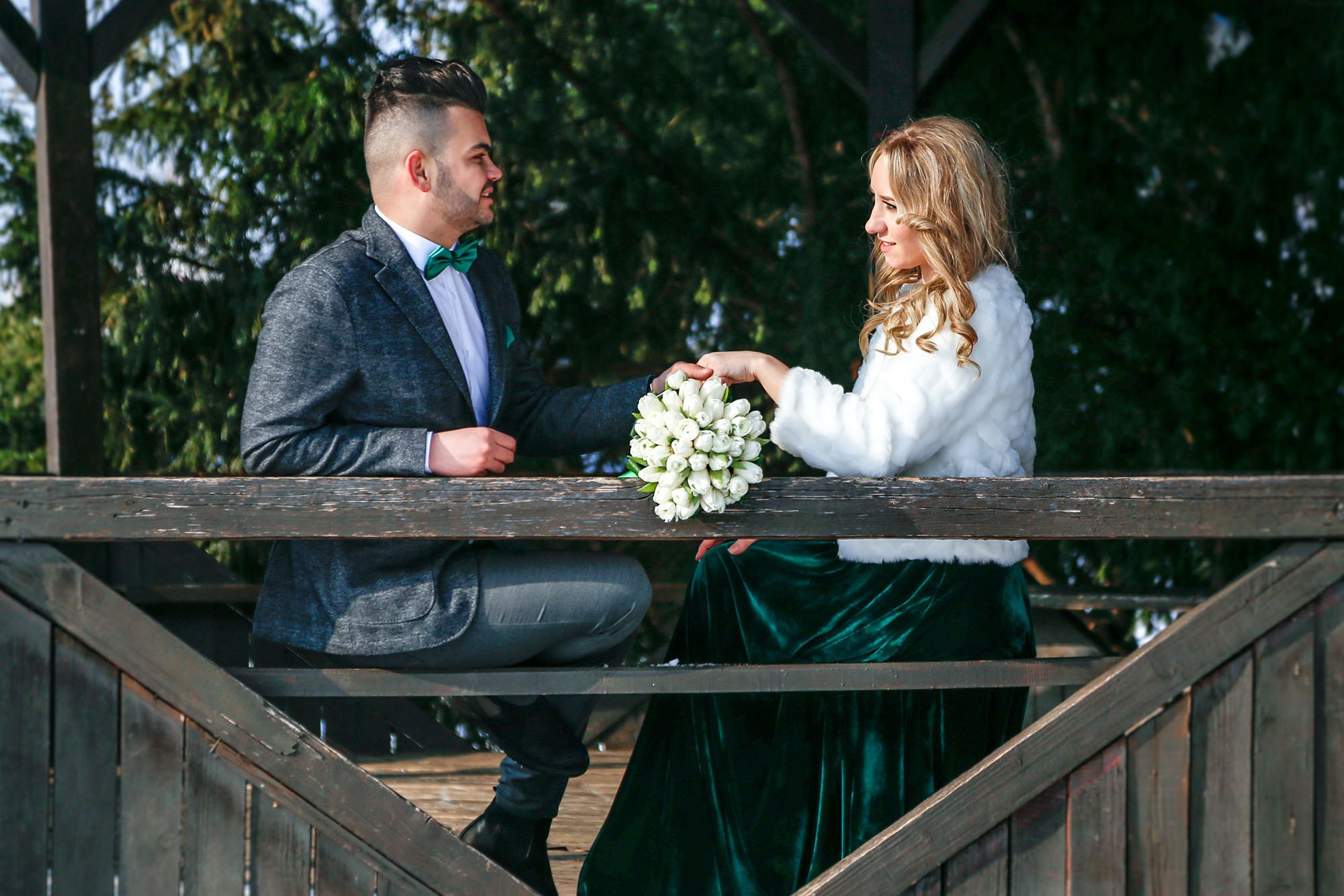 Candid shot of the newlyweds chatting and smiling inside the wooden gazebo, sharing a warm moment during the cold season.