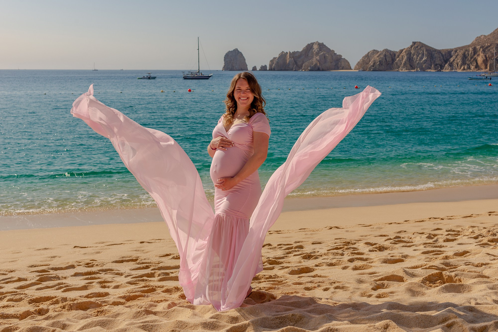 Los Cabos maternity photographer – elegant portrait of expecting mother in a dress flowing in the wind, highlighting the love, strength, and beauty of pregnancy by the sea