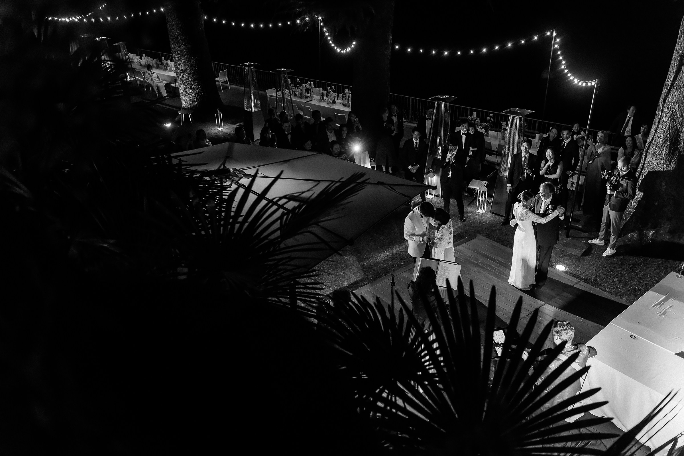 Elevated view of the wedding reception with guests seated under string lights, dancing couples in the center.