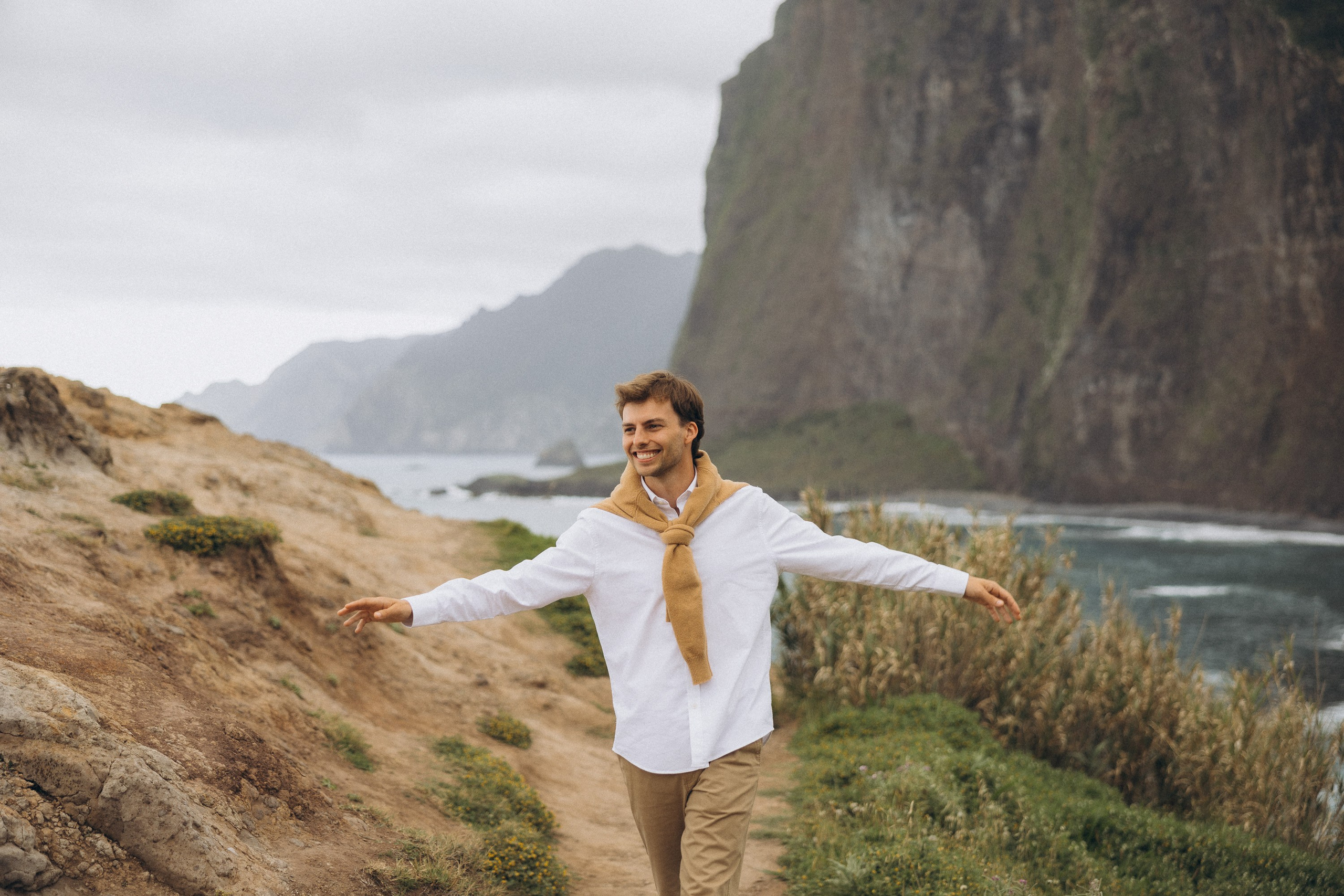 Beautiful engagement moment by the ocean in Madeira, Portugal, as one partner kneels to propose while waves crash in the background.