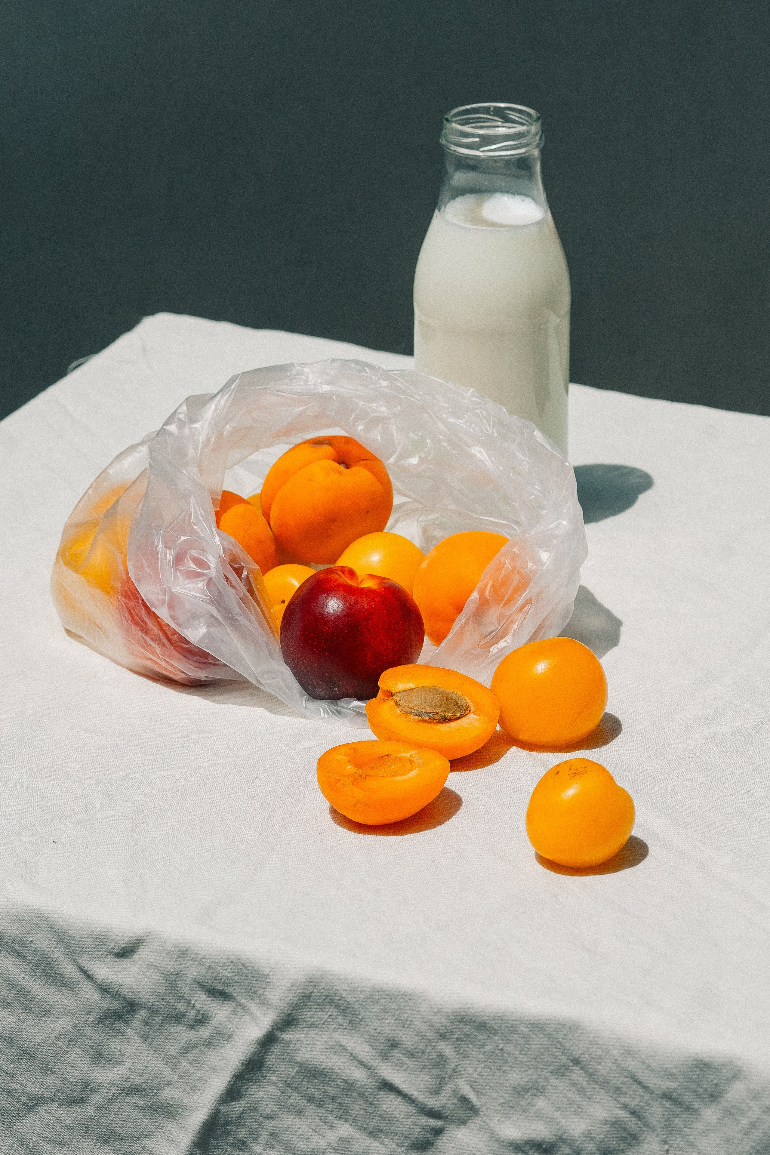 Fruit in a plastic bag with a bottle of milk. Apricots and peaches in a plastic bag near a bottle of milk placed on a table covered with a white tablecloth. 