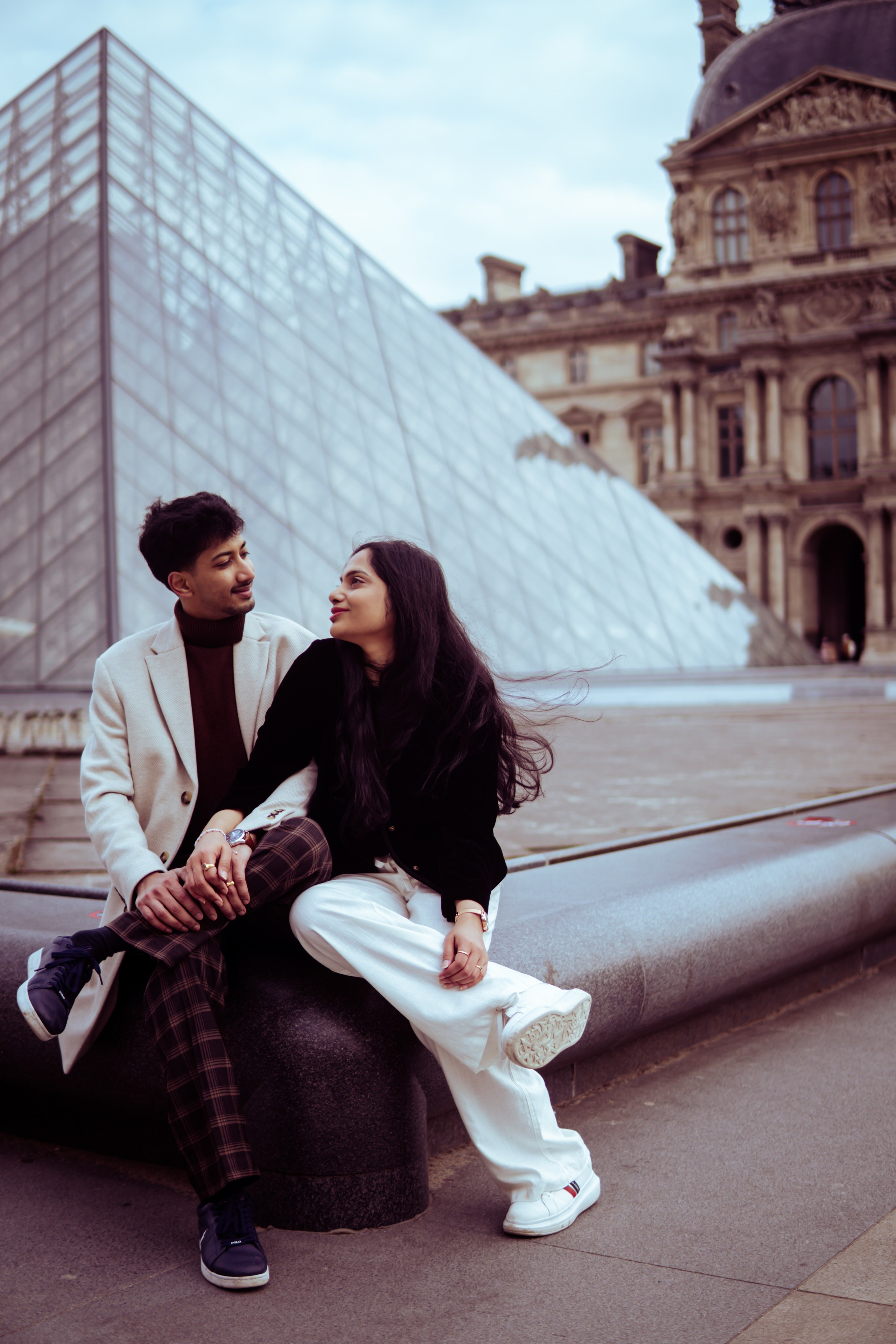 couple sitting in front of louvre museum