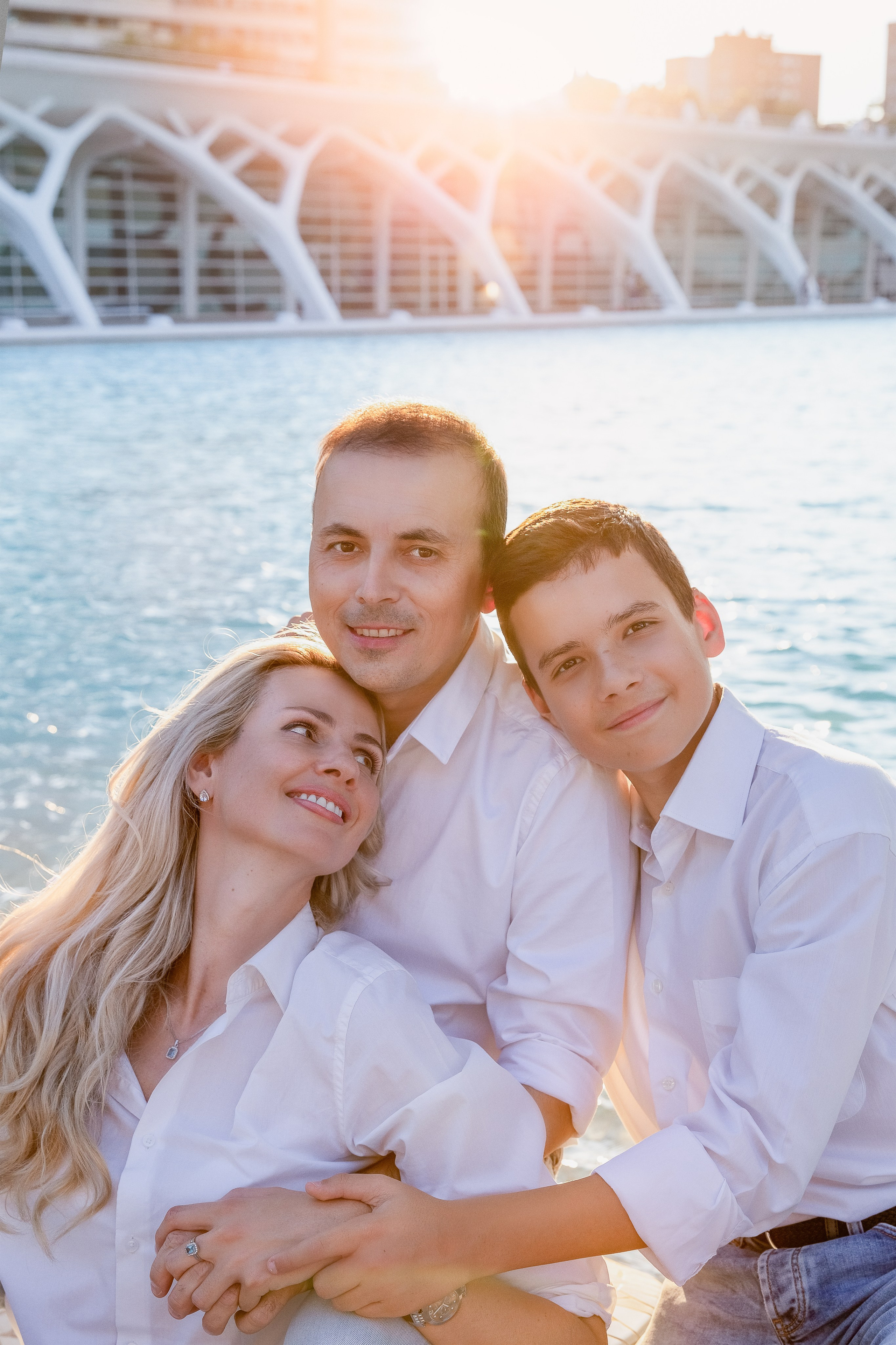 Retrato familiar al atardecer en Valencia, España, con un trío amoroso vestido de blanco junto a la Ciudad de las Artes y las Ciencias. Una sesión familiar elegante y atemporal perfecta para quienes buscan experiencias fotográficas emotivas en España.