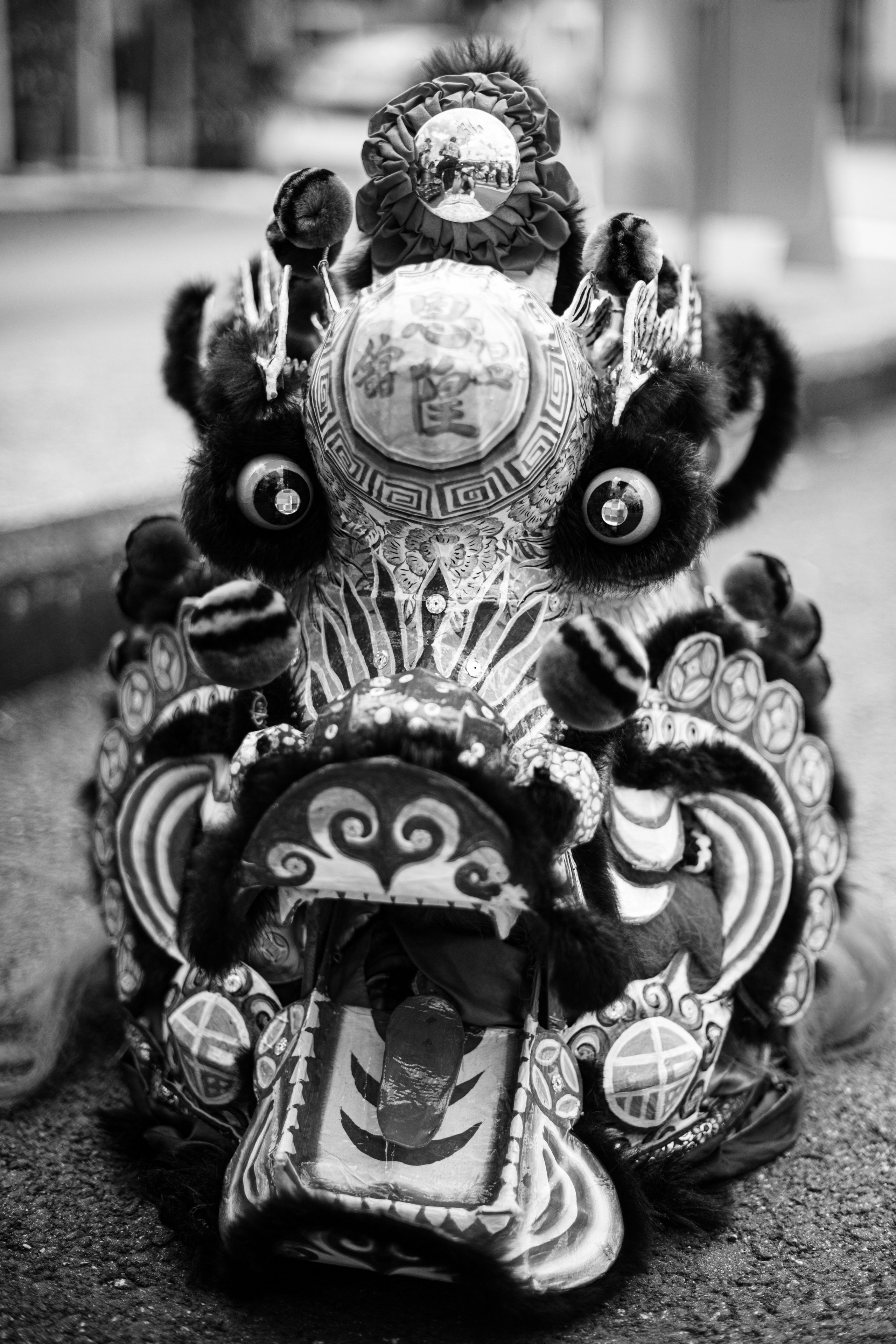 A detailed black-and-white close-up of an intricately designed lion dance head, resting on the pavement during the Monkey King’s Birthday celebration in Singapore. The ornate patterns and textures showcase the artistry and cultural significance of the performance. This image demonstrates the photographer’s skill in capturing the essence of cultural events with precision and storytelling, ideal for clients looking for immersive event or photojournalism coverage.