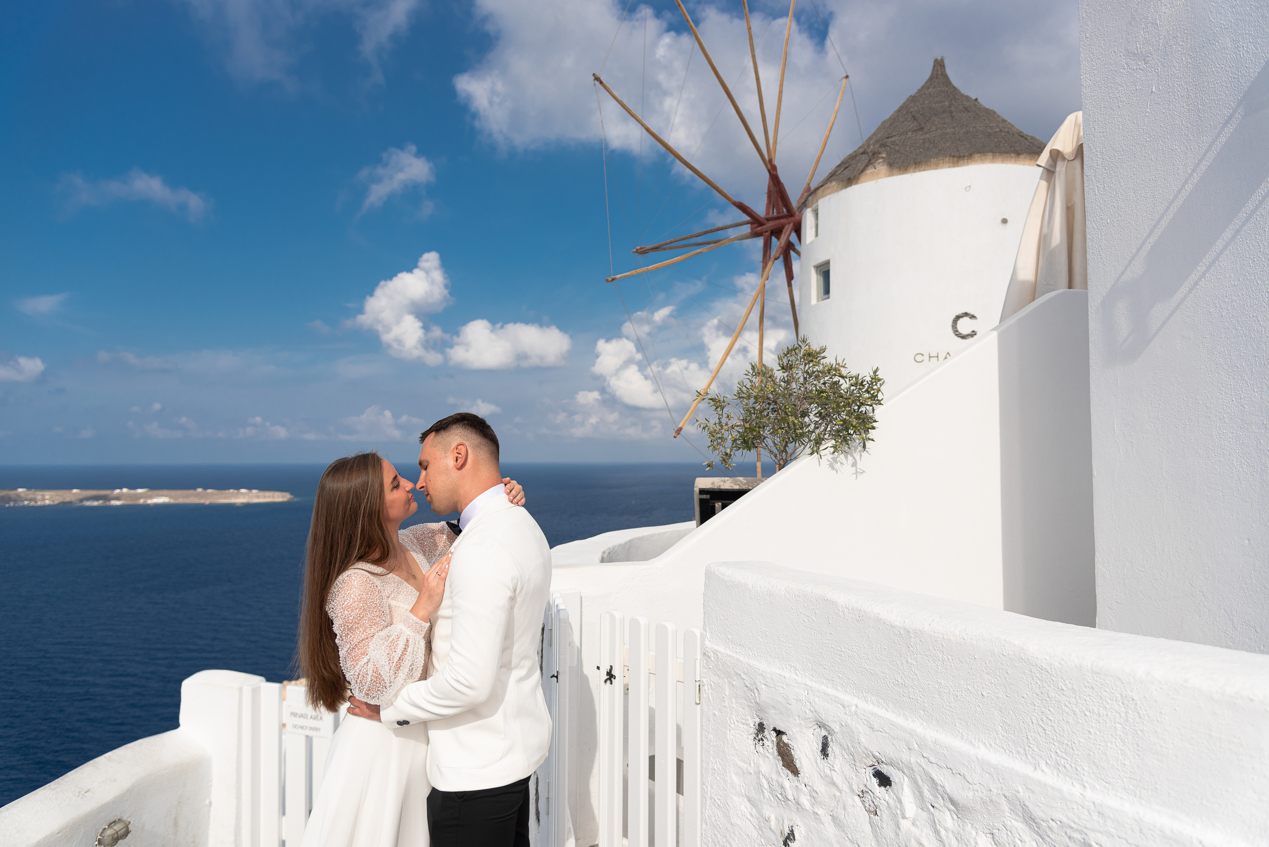 The bride and groom kiss against the background of a windmill and a view of the sea