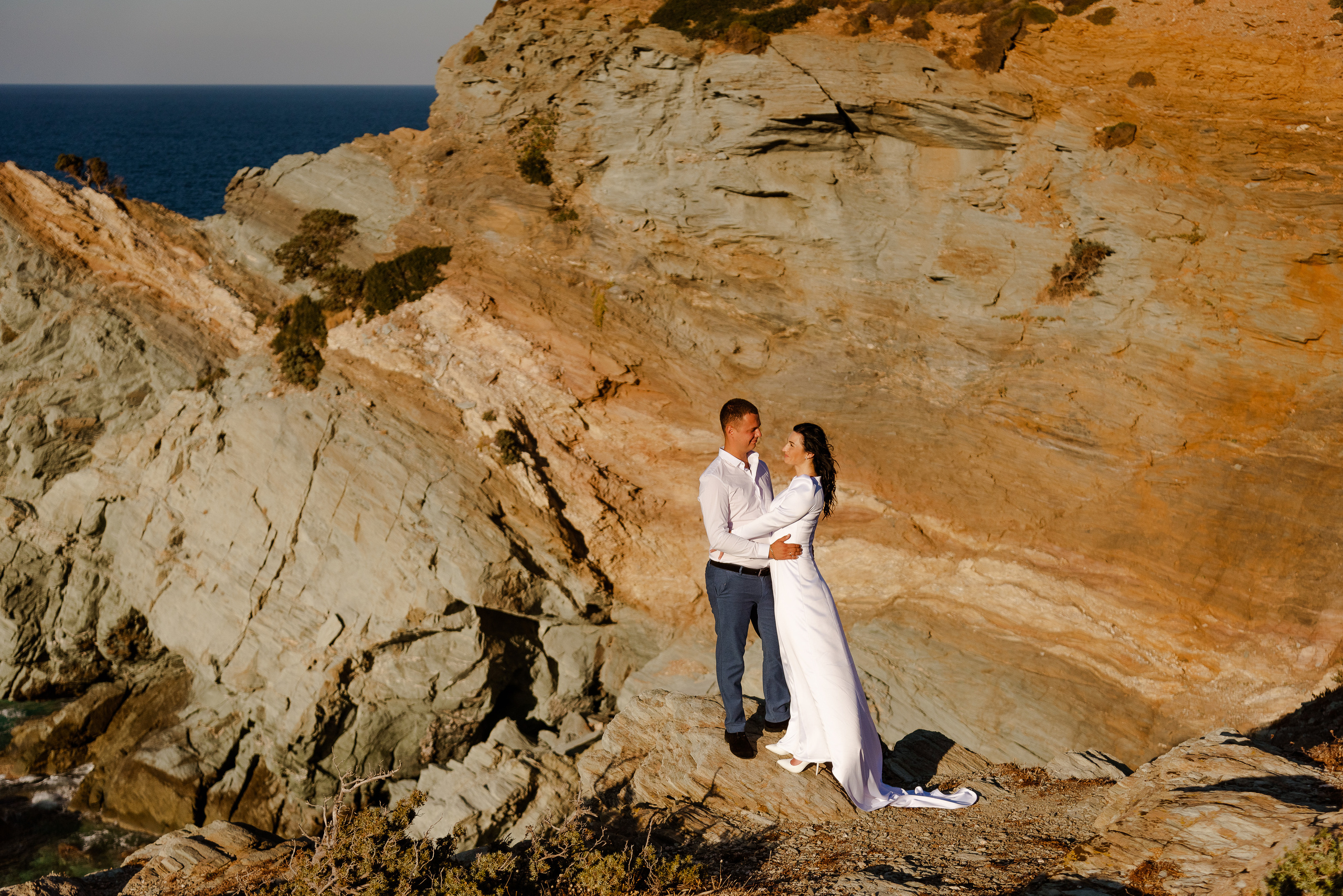 The newlyweds are standing on a mountain with a view of the sea and hugging