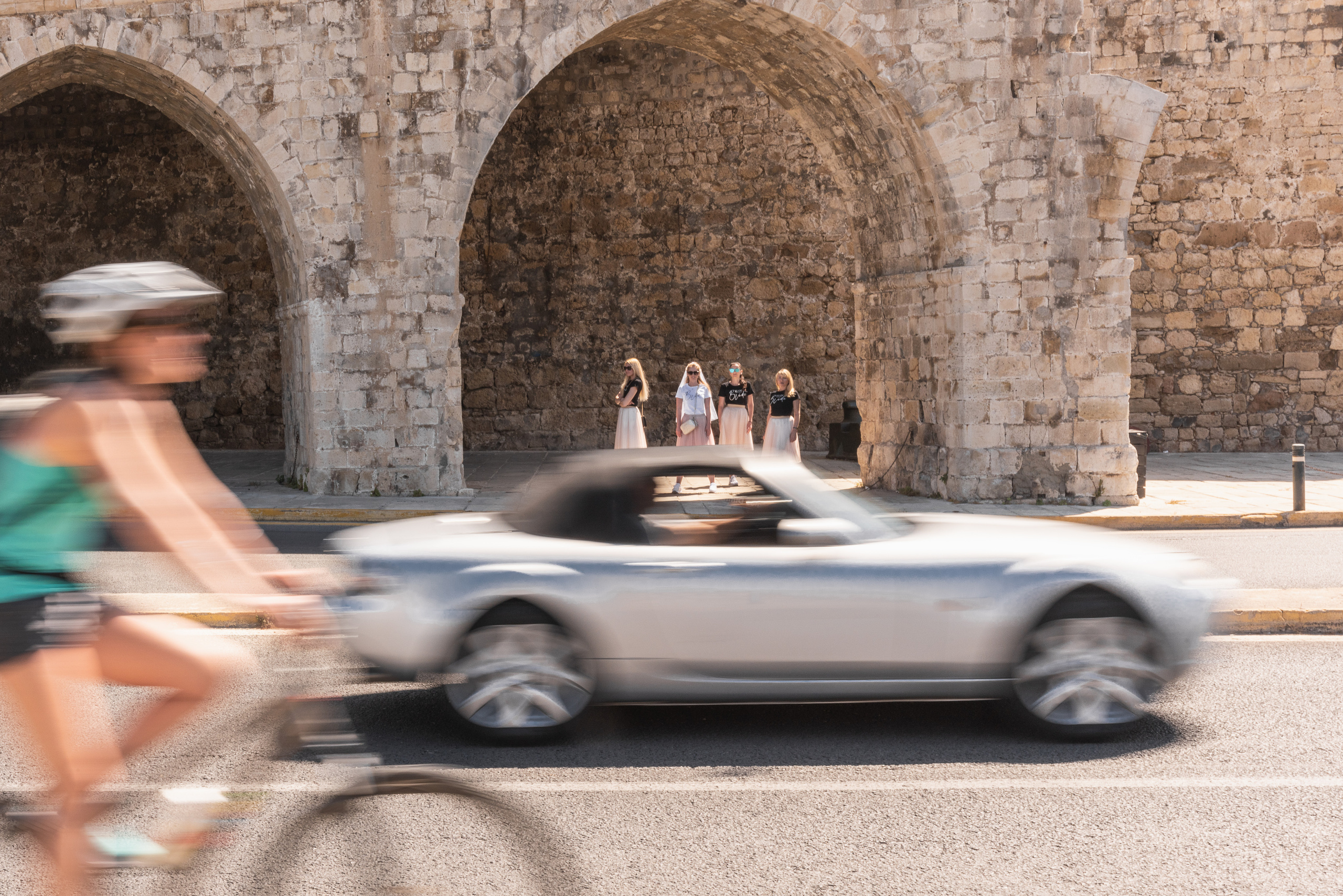 Wedding photo shoot of friends from the old town, in the foreground a bicycle and a car are riding fast