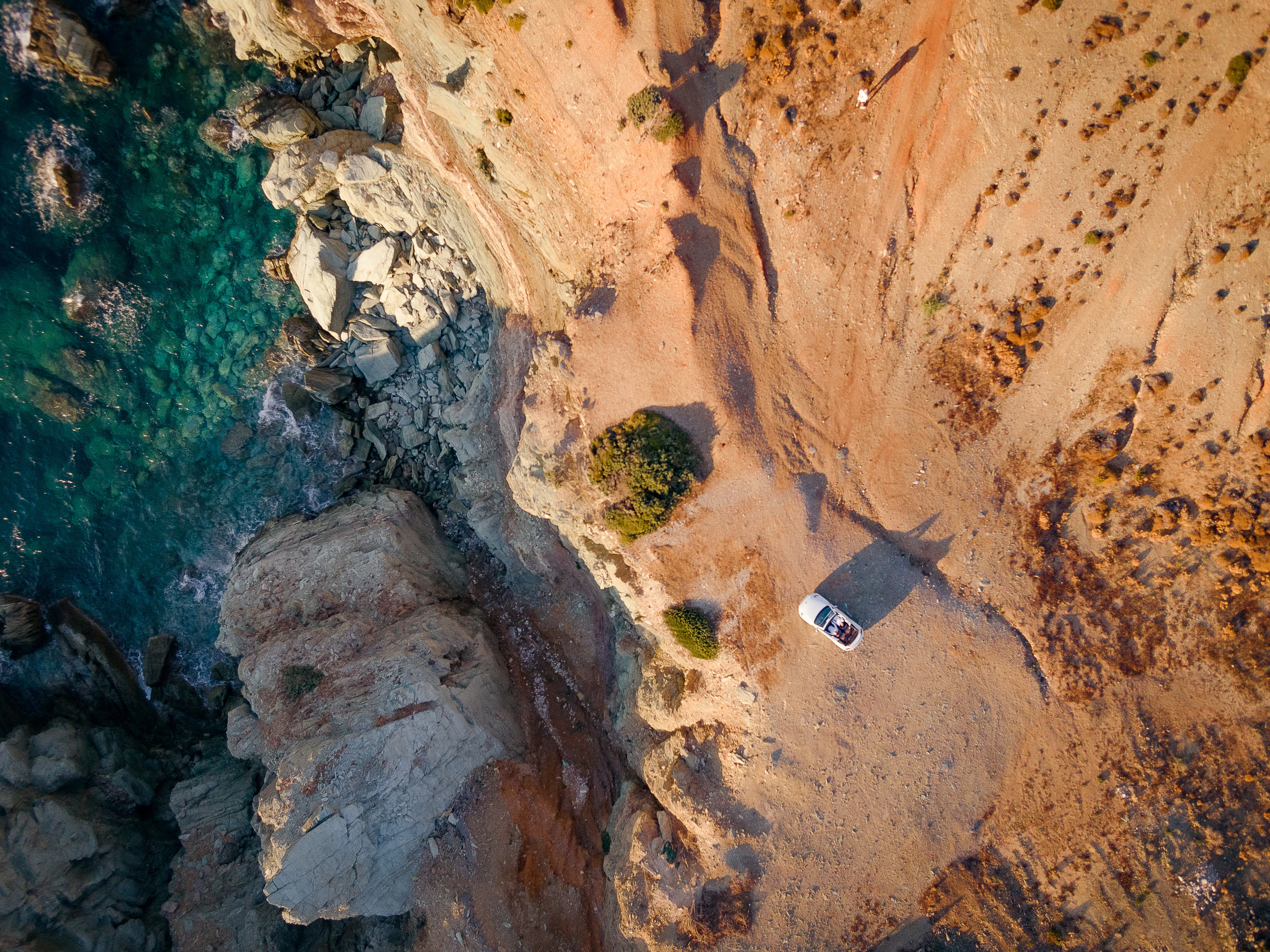 A white convertible is standing on a cliff by the sea at sunset