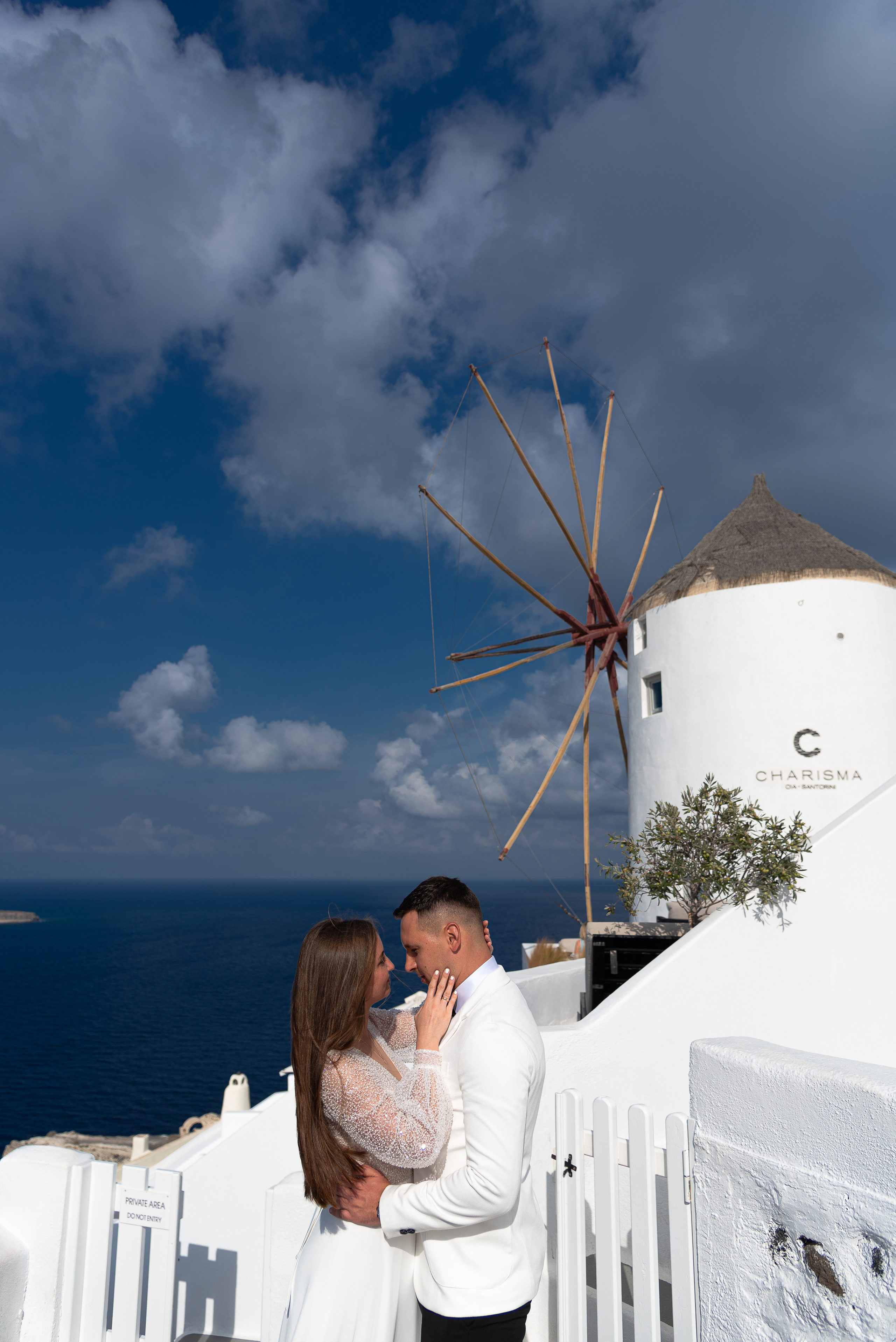 The bride and groom kiss against the background of a windmill and a view of the sea