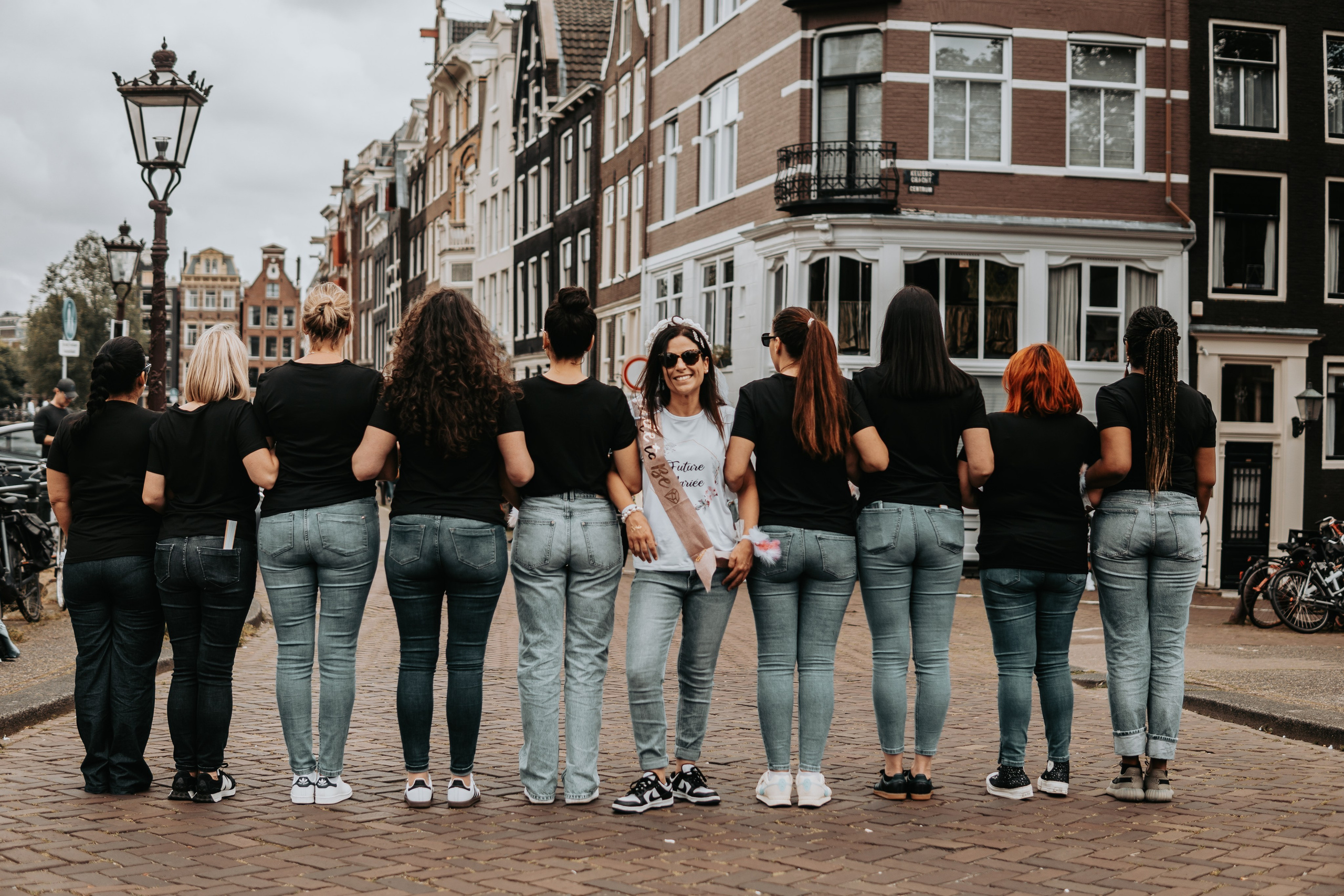 bride to be facing one way and her girl friends facing the other way and standing on a canal bridge in amsterdam
