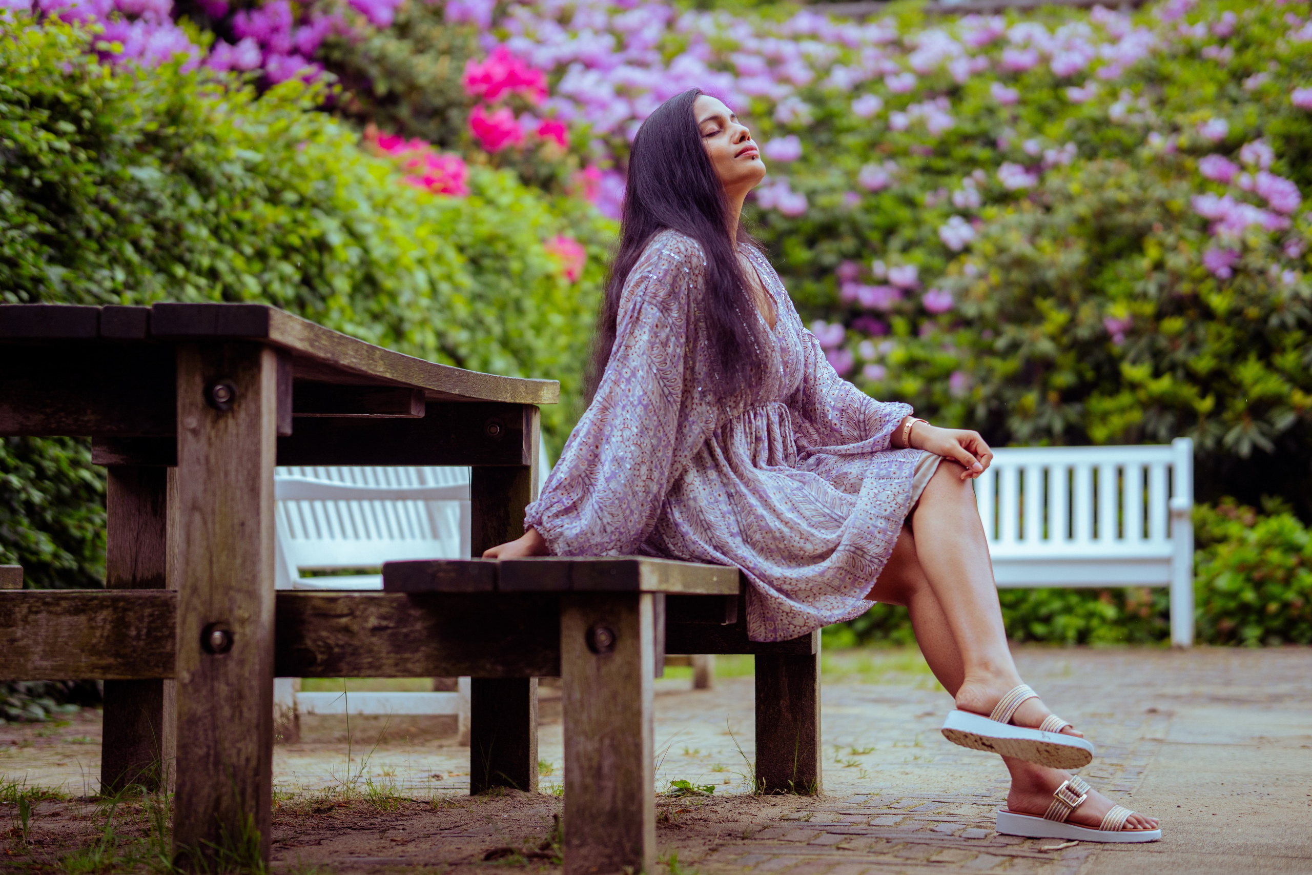 woman sitting on a white bench with flowers as background