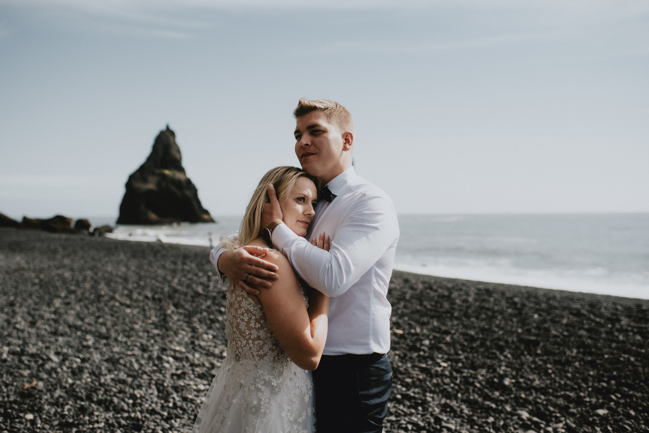Newlyweds walking hand in hand along the shoreline of Reynisfjara, with dramatic waves crashing behind them.