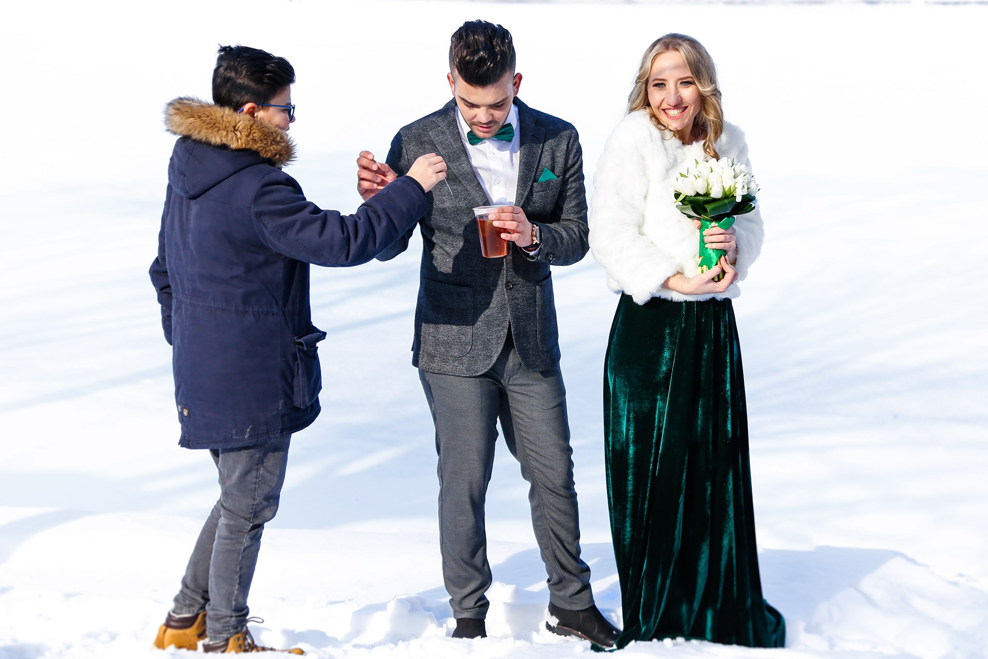 The groom's brother bringing hot tea to the newlyweds to keep them warm, a relaxed and caring moment captured during the winter photo shoot.
