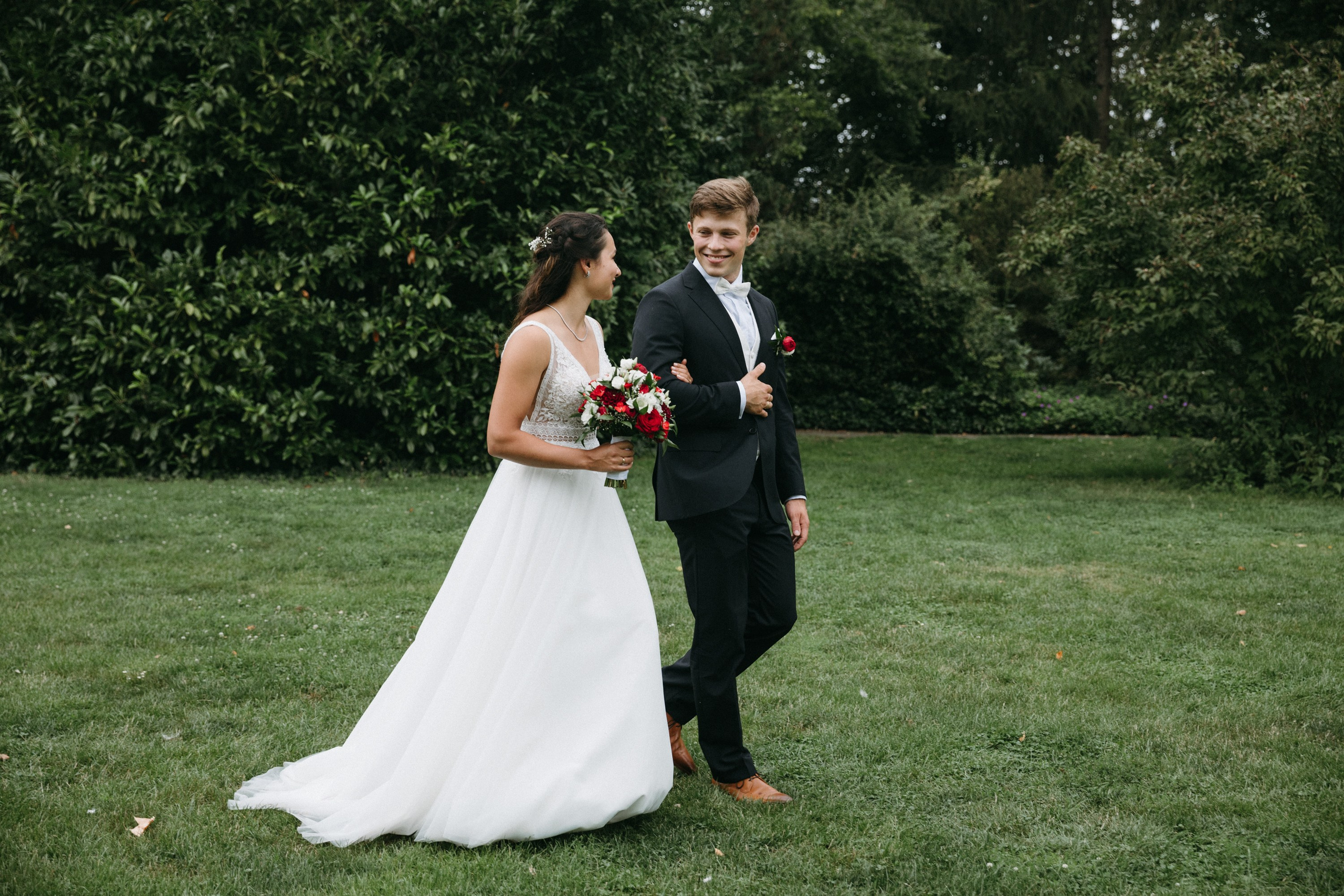 Braut und Bräutigam gehen über Rasen, lächeln sich gegenseitig an