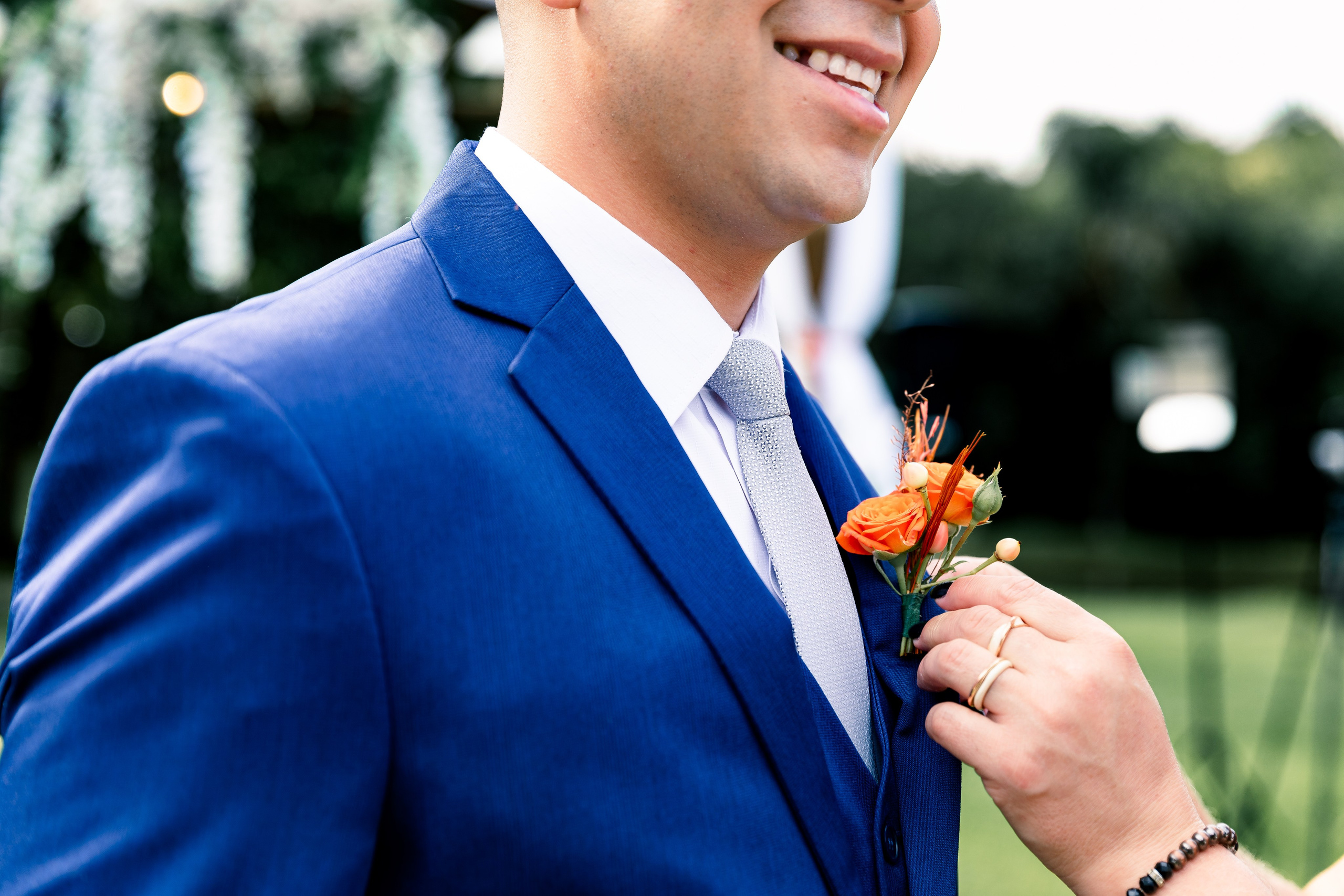 Noivo sorrindo em espera da noiva, enquanto a cerimonialista ajeita a sua lapela no peito