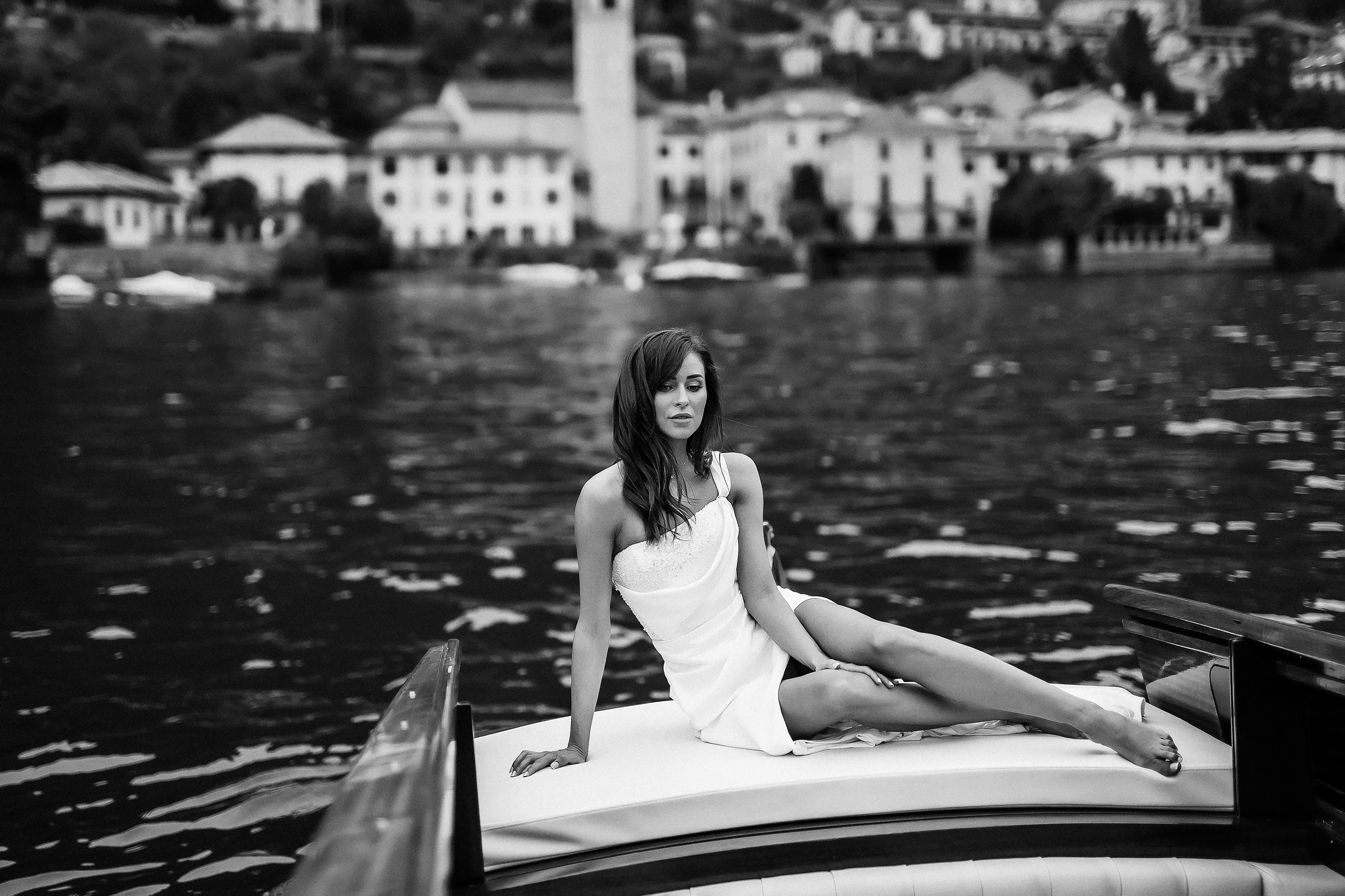 Timeless black and white portrait of the bride in white dress on boat, with historic lakeside town and clock tower in the background.