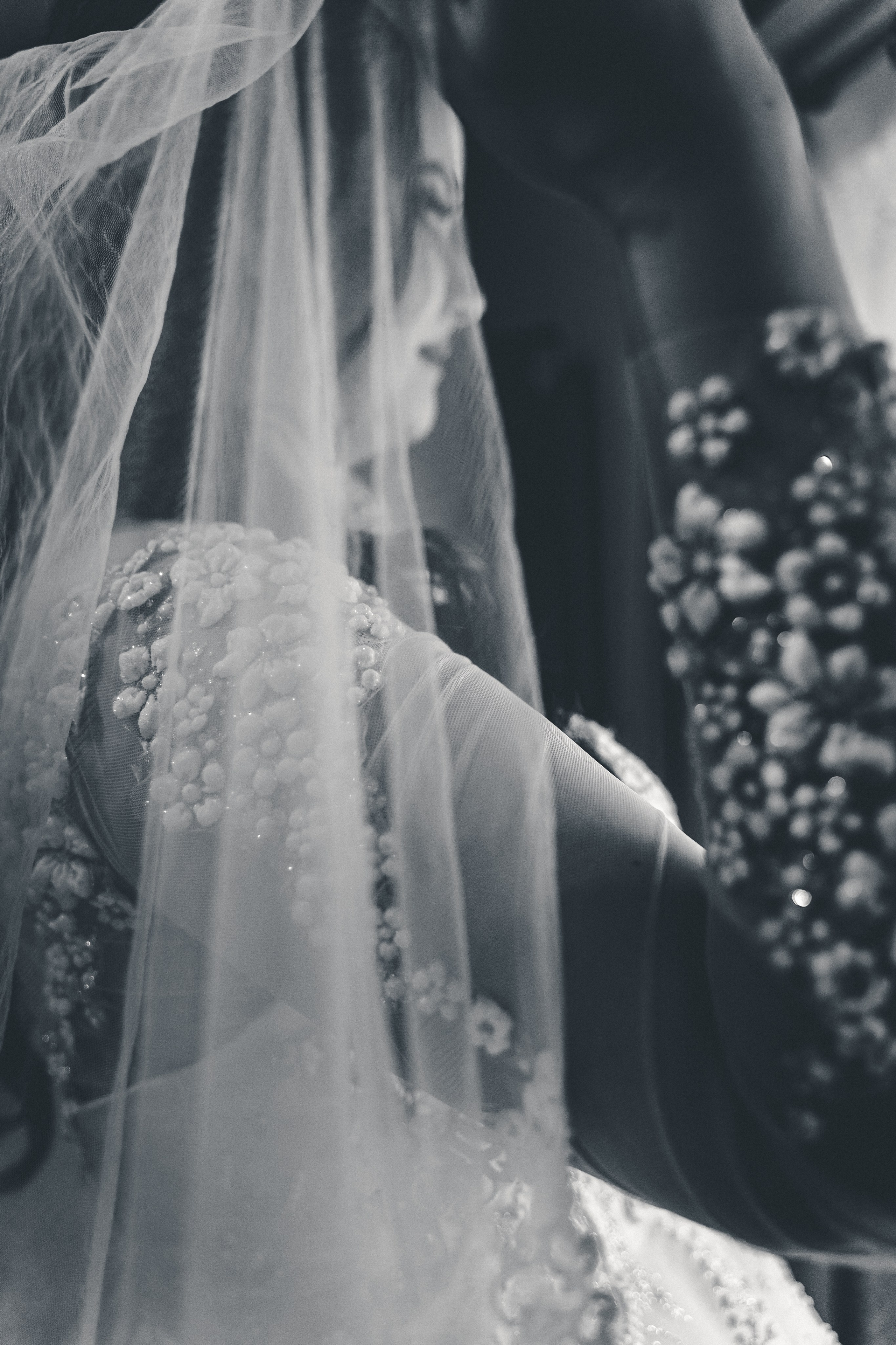 Detaliu alb-negru cu văl de mireasă transparent și mâneca rochiei decorată cu perle și flori 3D, incadru.ro.