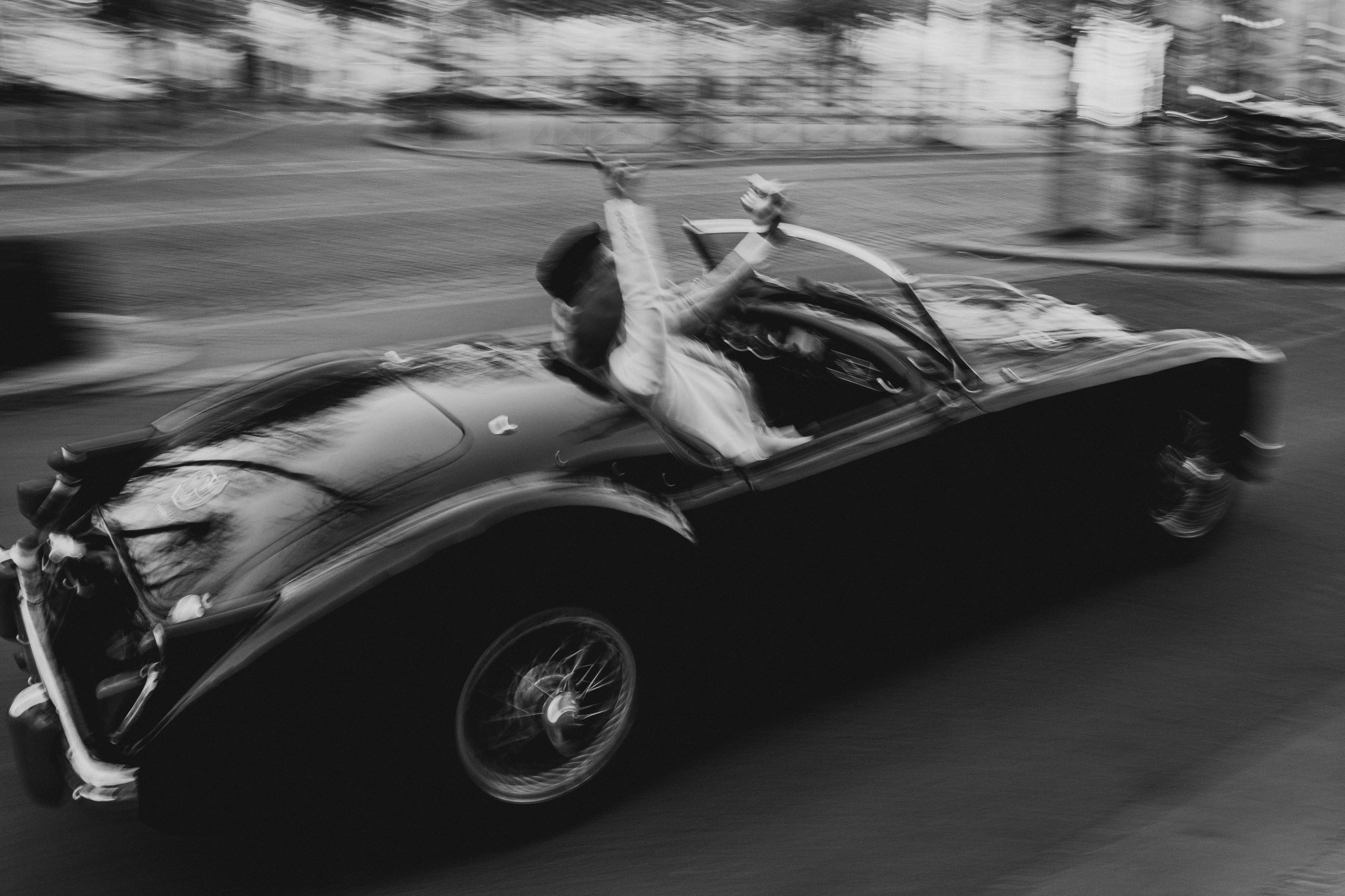 Joyful wedding celebration in a vintage car driving through Paris, black and white Paris wedding photography with cinematic motion