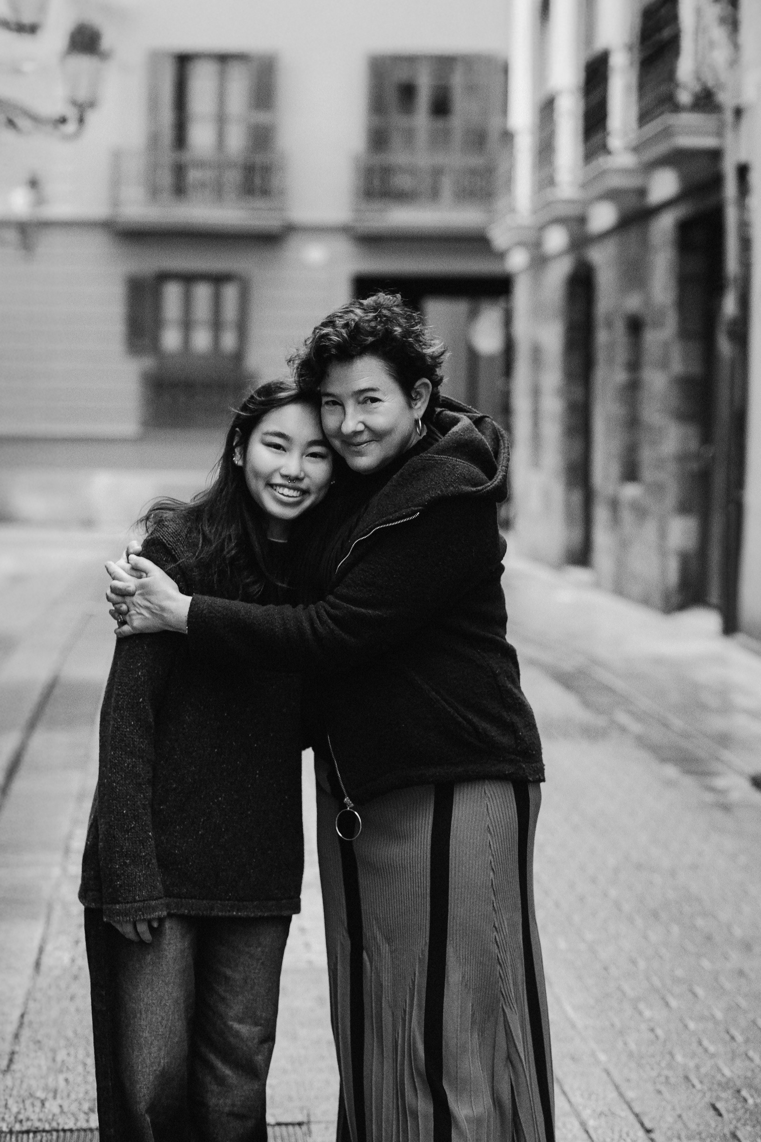 Семейная фотосессия в Валенсии, Испания, где улыбающаяся пара обнимается на очаровательной улице старого города, снято в чёрно-белом стиле для вневременного, искреннего и эмоционального момента — идеально для семейных и парных фотосессий в Валенсии и по всей Испании.