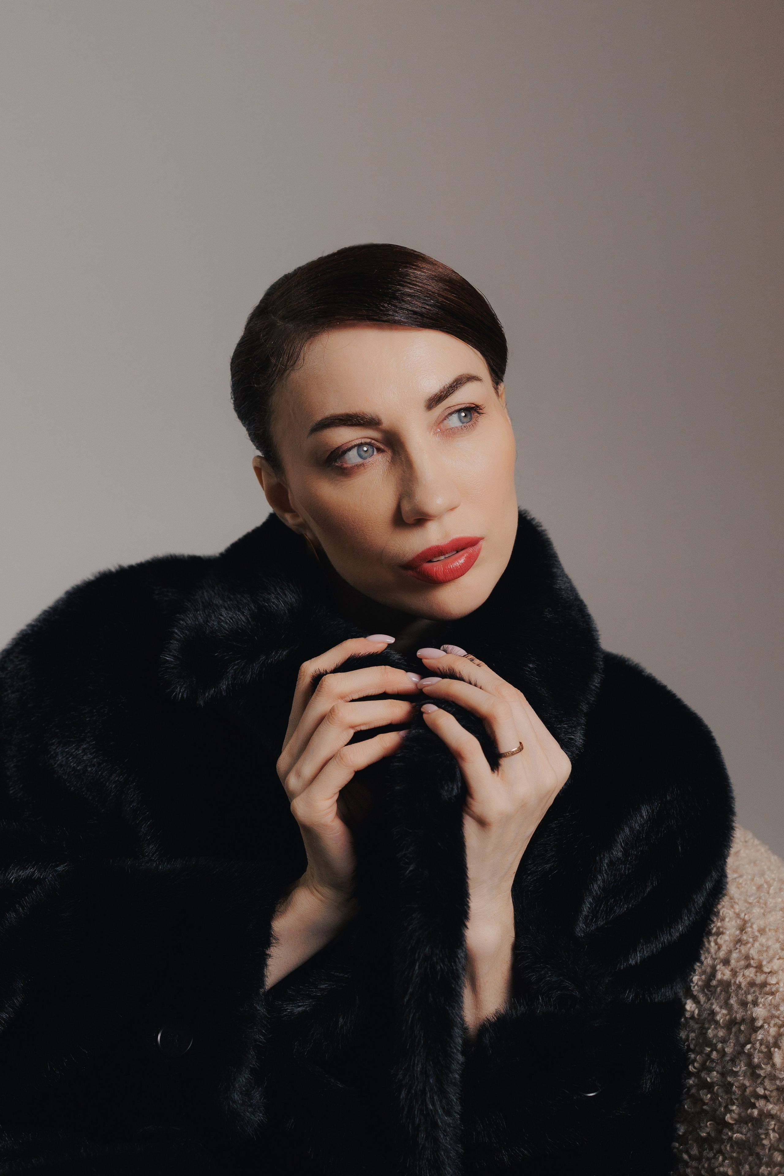 Elegant editorial studio portrait of a woman in a black fur coat with hands near her face and dramatic lighting, photographed in Leipzig, Germany. Элегантный редакционный студийный портрет девушки в чёрной шубе с руками возле лица и драматичным освещением, снятый в Лейпциге, Германия.