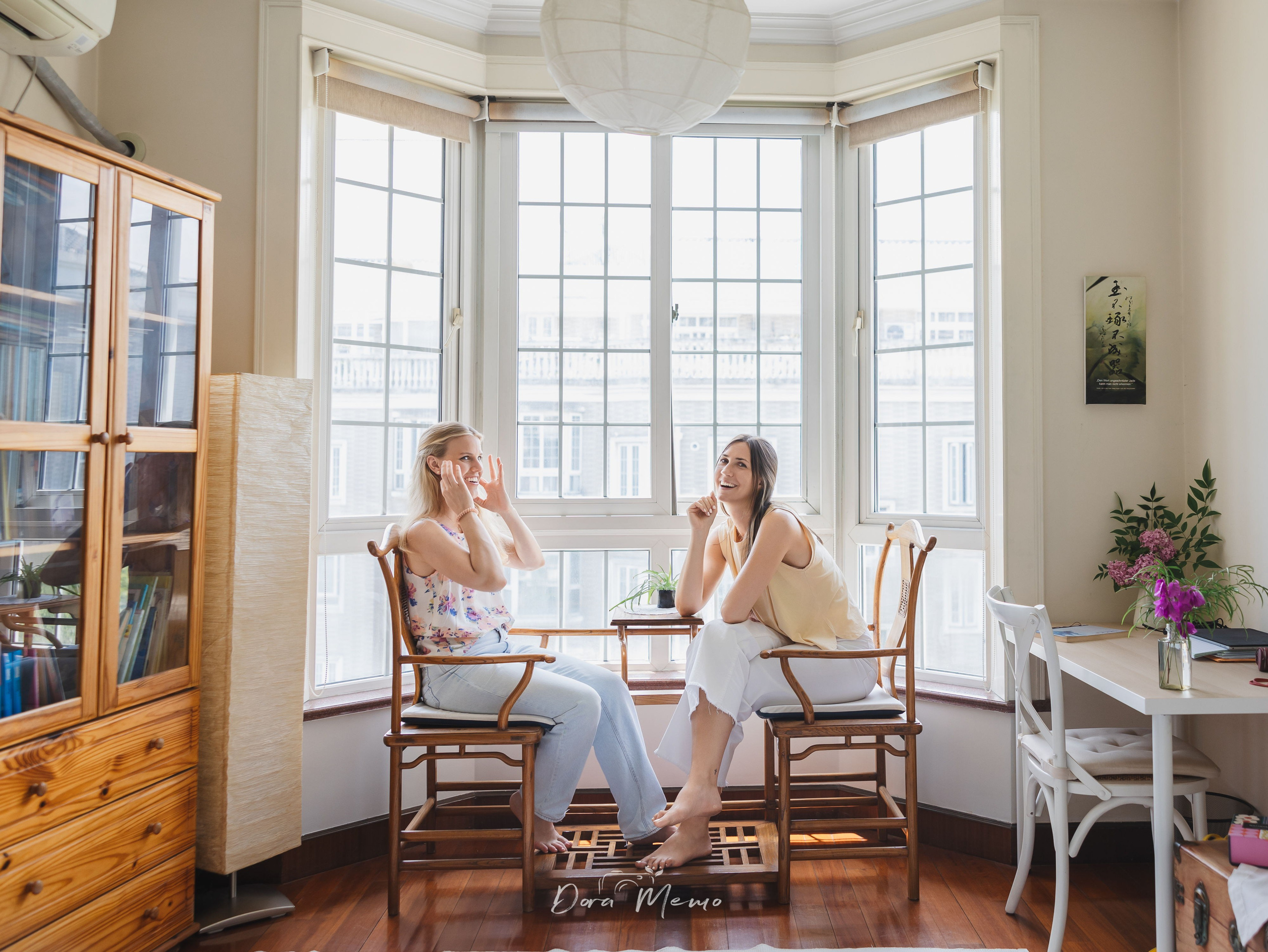 Two sisters sitting near Chinese chairs in a bright Shanghai apartment.
