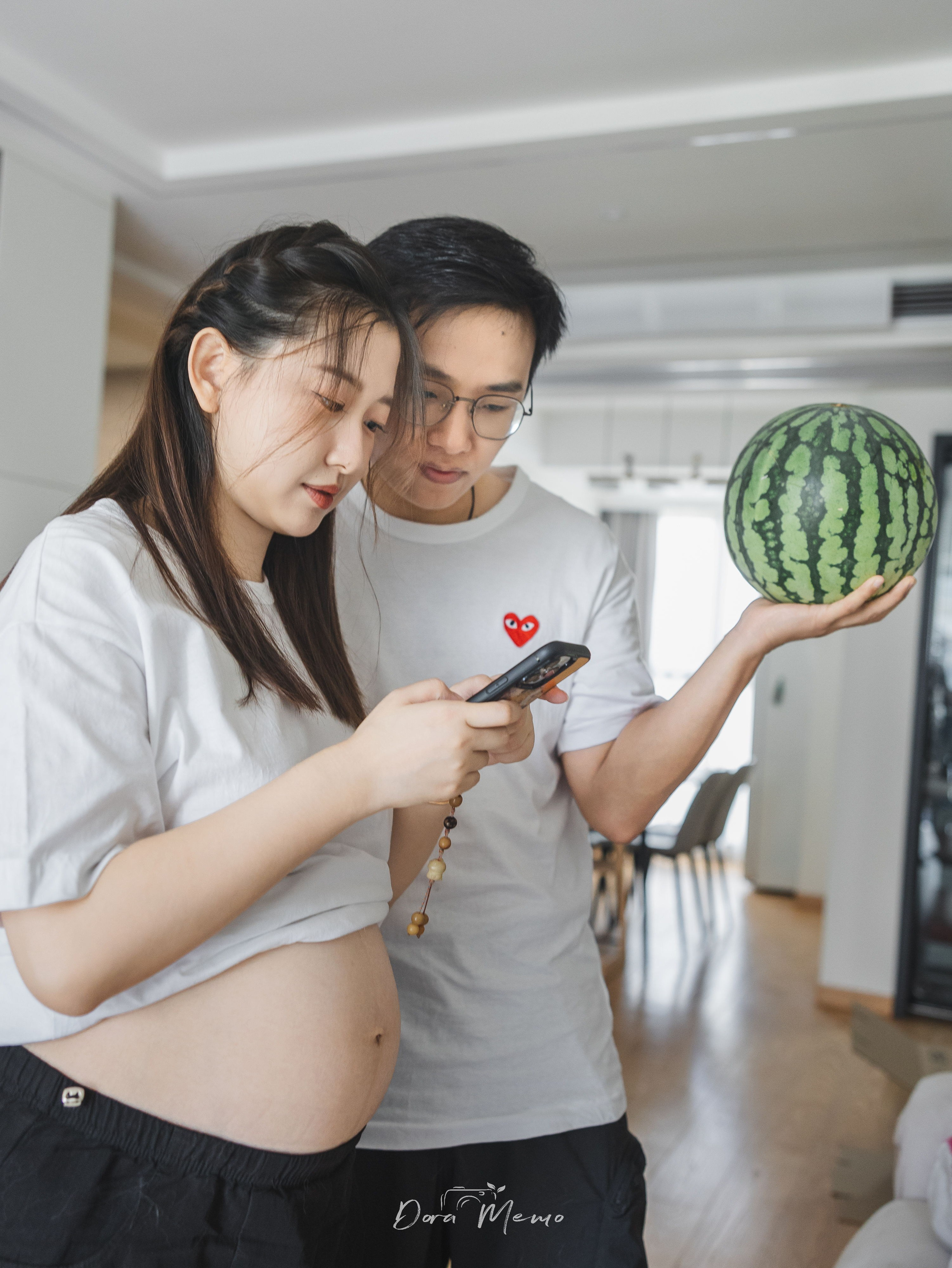 A playful maternity photo with expecting parents holding watermelon beside the baby bump.