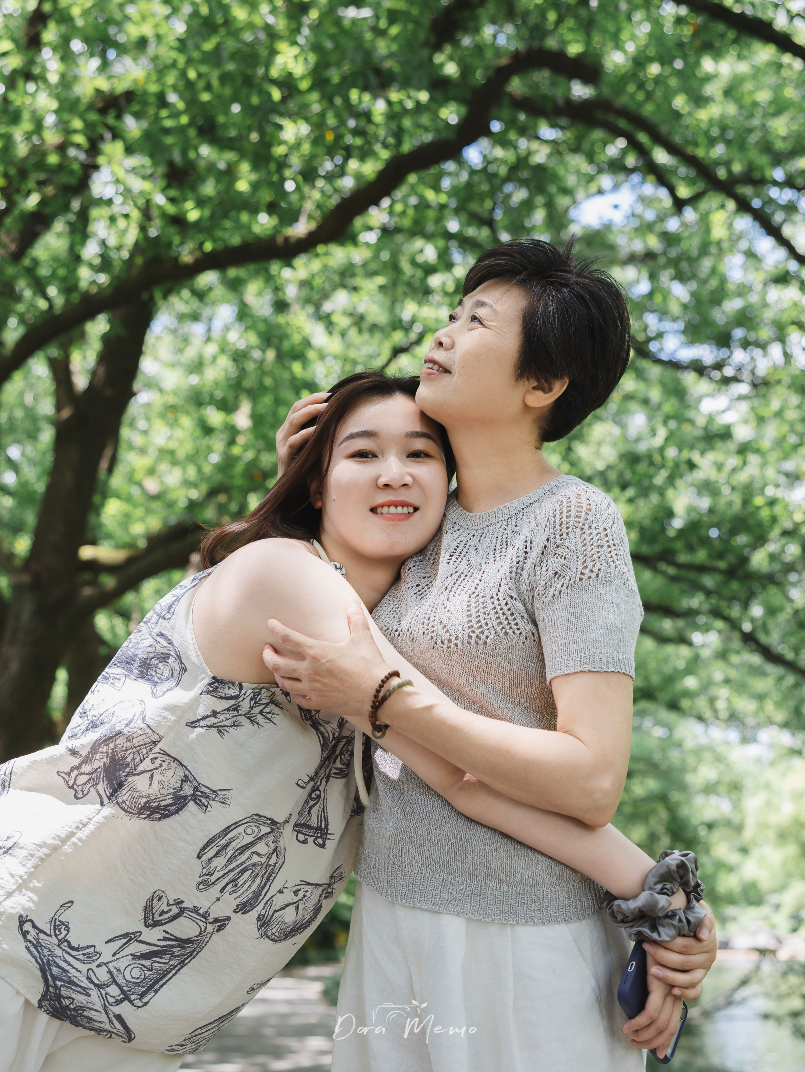A mother and grandmother embrace beneath the trees during a three-generation family session.